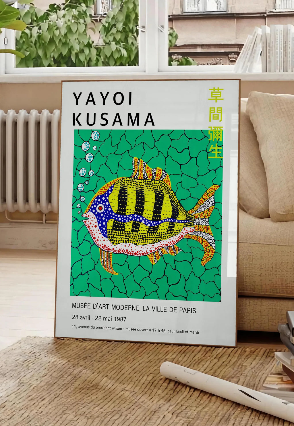 Poster affiche poisson a pois de Kusama art japonais, posee au sol dans un salon parisien, devant une grande fenetre donnant sur un immeuble haussmannien, entre un ficus et un canape creme