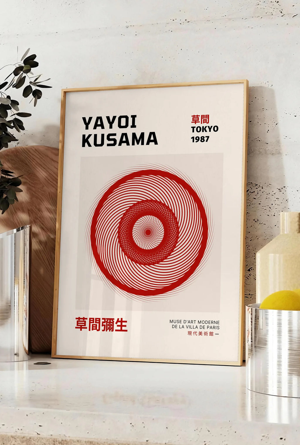 Affiche affiche spirale rouge de Kusama art japonais, posee sur un plan de travail de cuisine en pierre claire, entre une branche d'eucalyptus en vase et un bocal de citrons