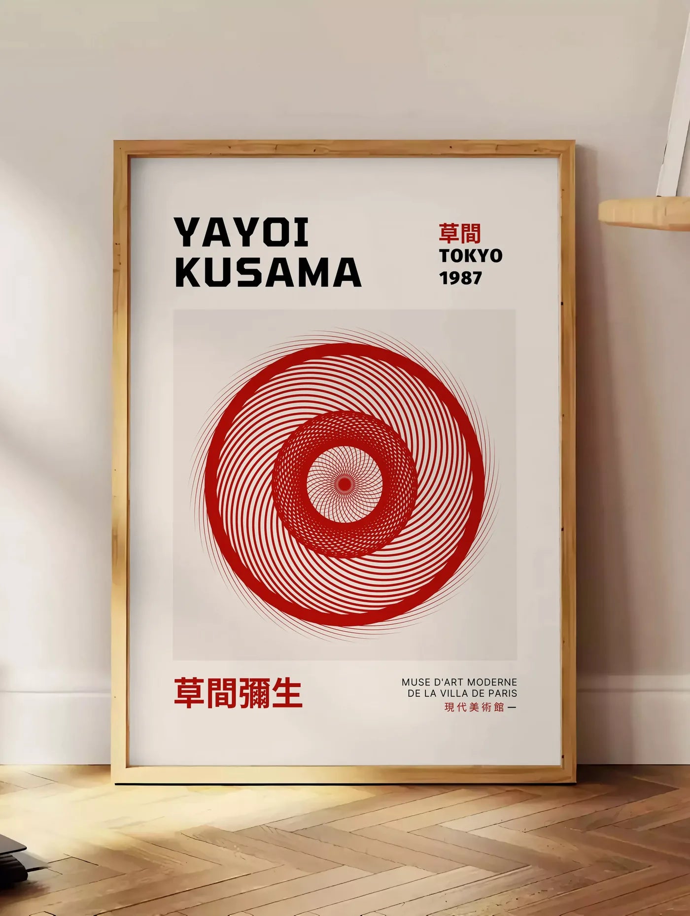 Estampe affiche spirale rouge de Kusama art japonais, posee au sol dans un coin salon, sur un parquet a chevrons, pres d'une table d'appoint en chene chargee de livres