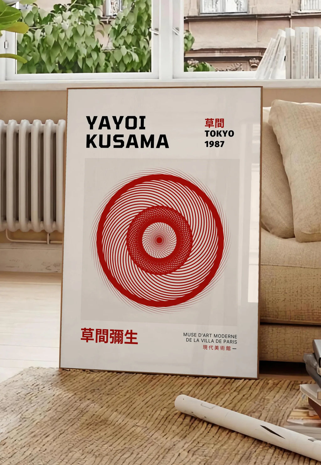 Poster affiche spirale rouge de Kusama art japonais, posee au sol dans un salon parisien, devant une grande fenetre donnant sur un immeuble haussmannien, entre un ficus et un canape creme