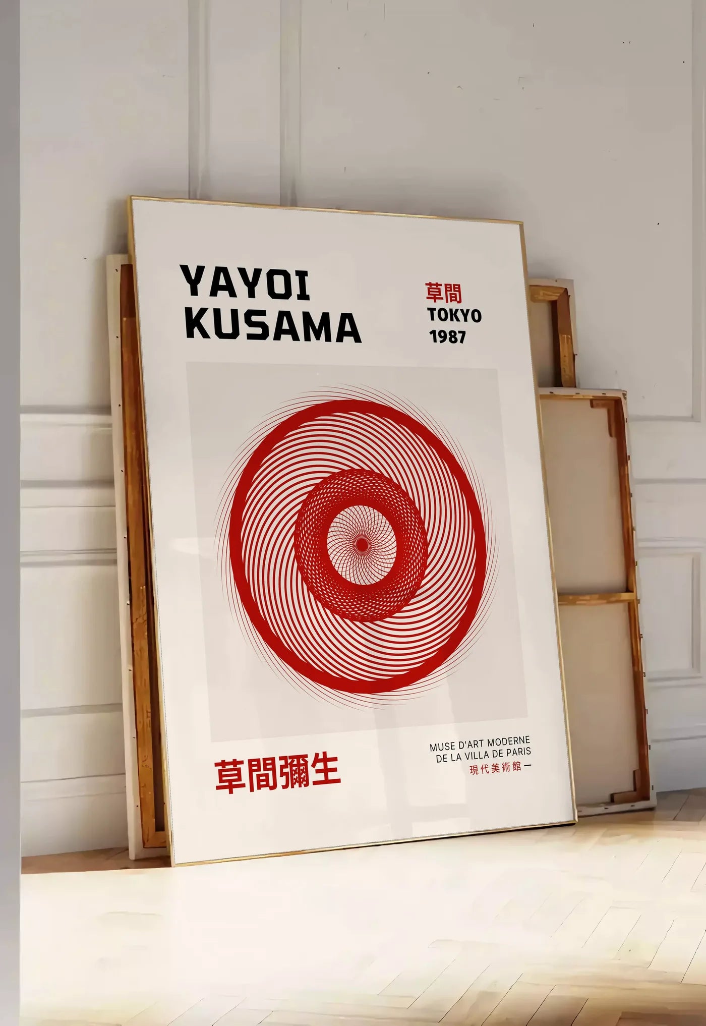 Tirage encadrable affiche spirale rouge de Kusama art japonais, posee au sol dans une entree lumineuse, contre un mur a panneaux blancs, a cote de chassis en bois empiles