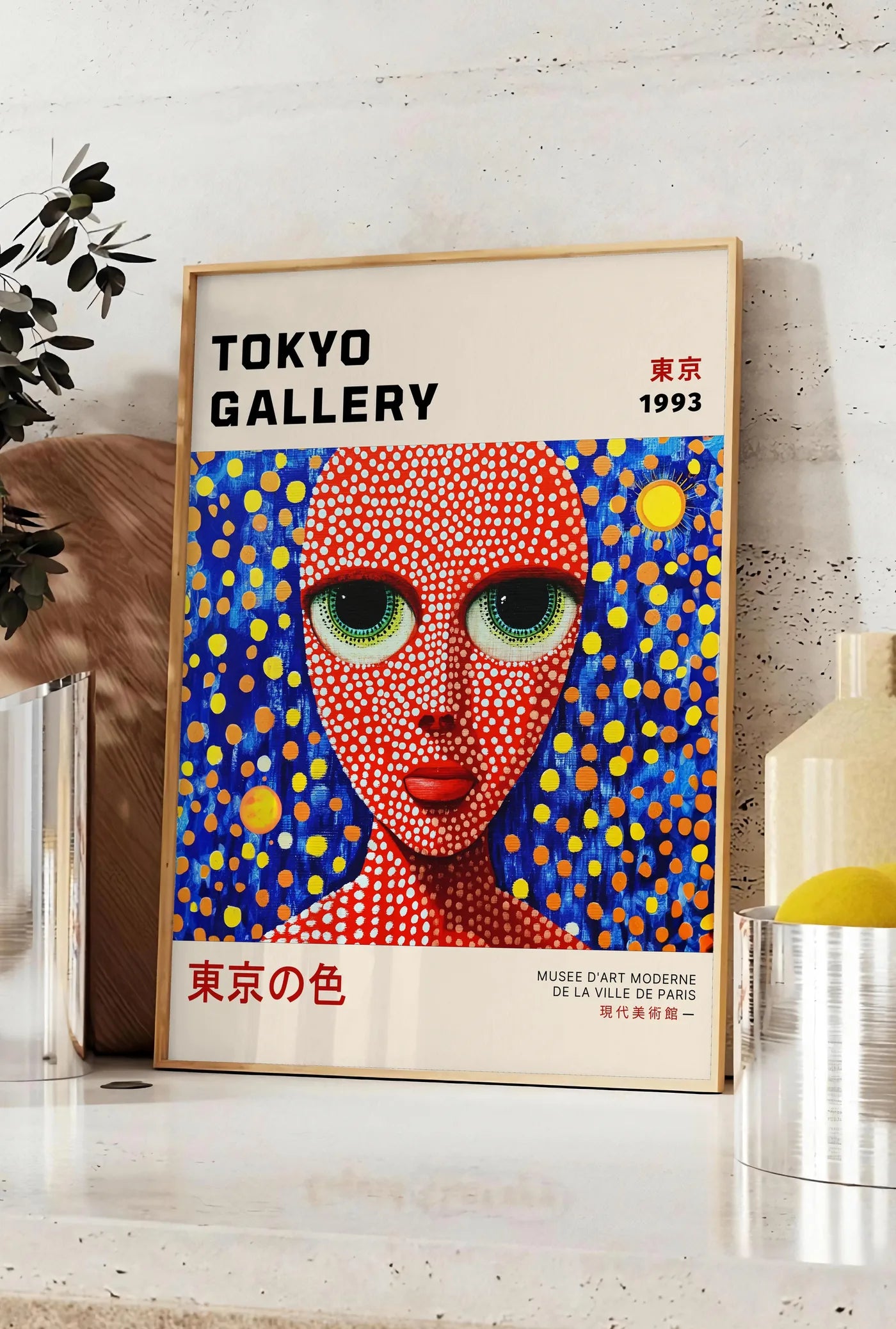 Affiche affiche visage de femme a pois de Kusama art japonais, posee sur un plan de travail de cuisine en pierre claire, entre une branche d'eucalyptus en vase et un bocal de citrons