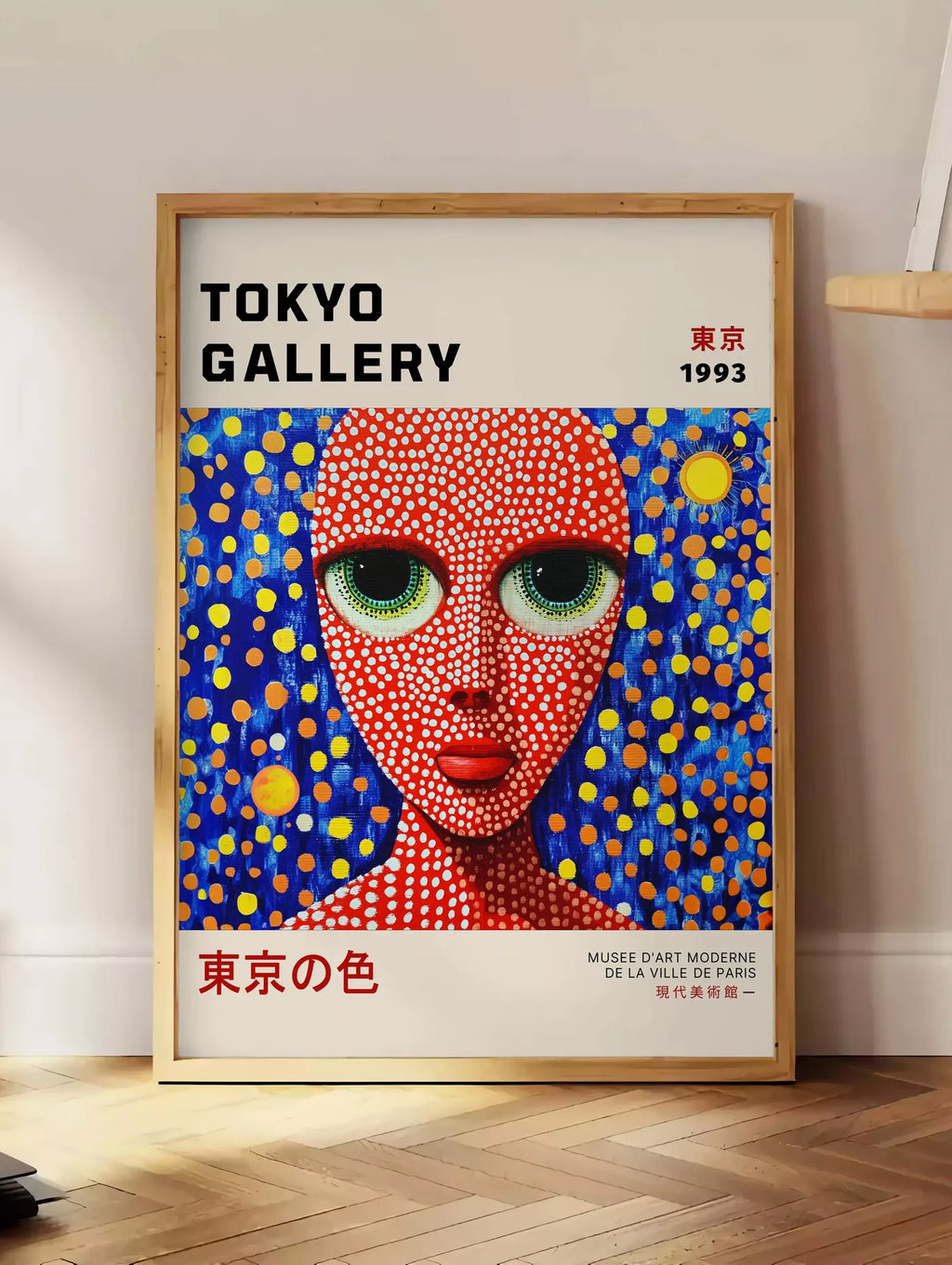 Estampe affiche visage de femme a pois de Kusama art japonais, posee au sol dans un coin salon, sur un parquet a chevrons, pres d'une table d'appoint en chene chargee de livres