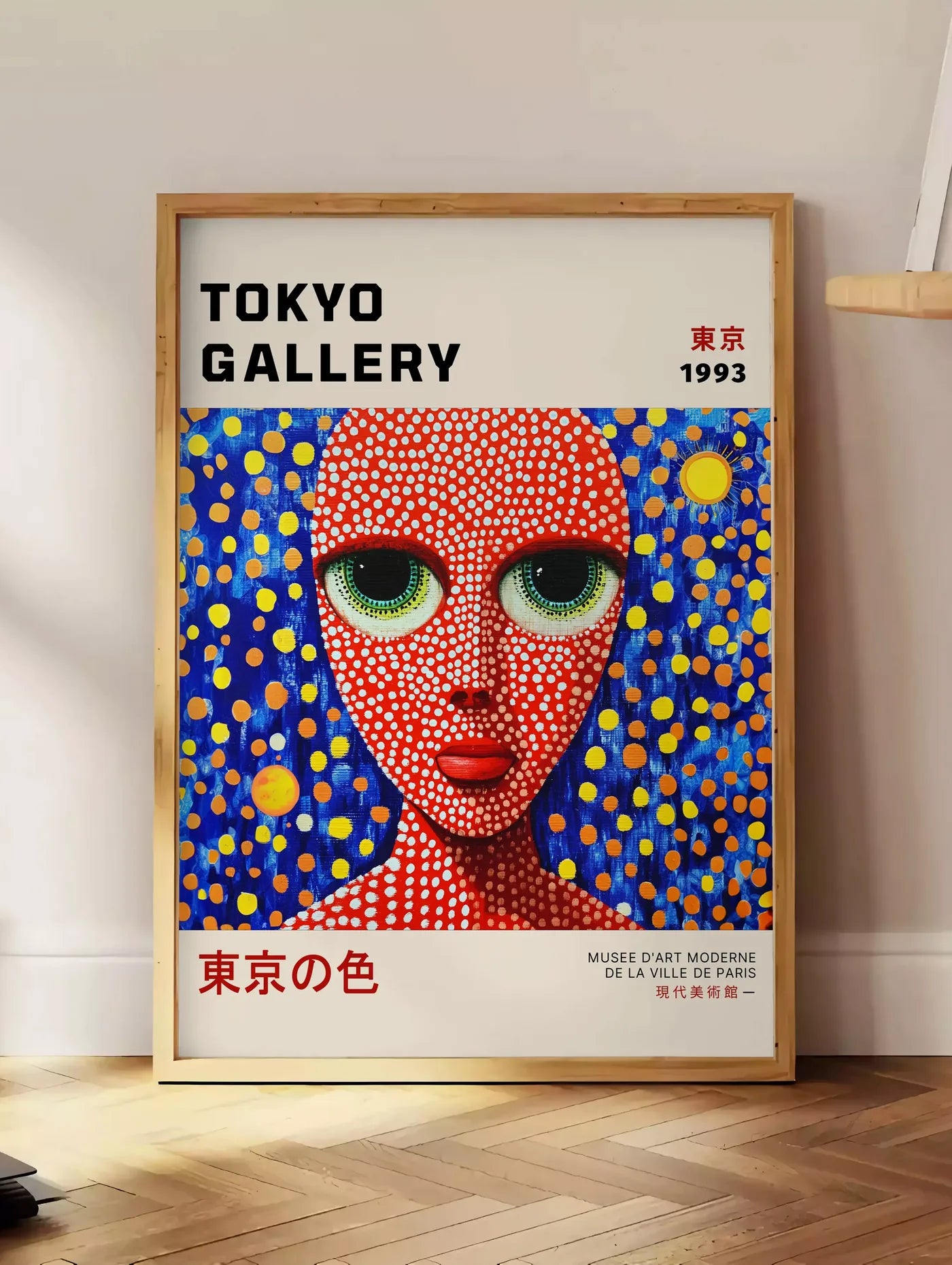 Estampe affiche visage de femme a pois de Kusama art japonais, posee au sol dans un coin salon, sur un parquet a chevrons, pres d'une table d'appoint en chene chargee de livres