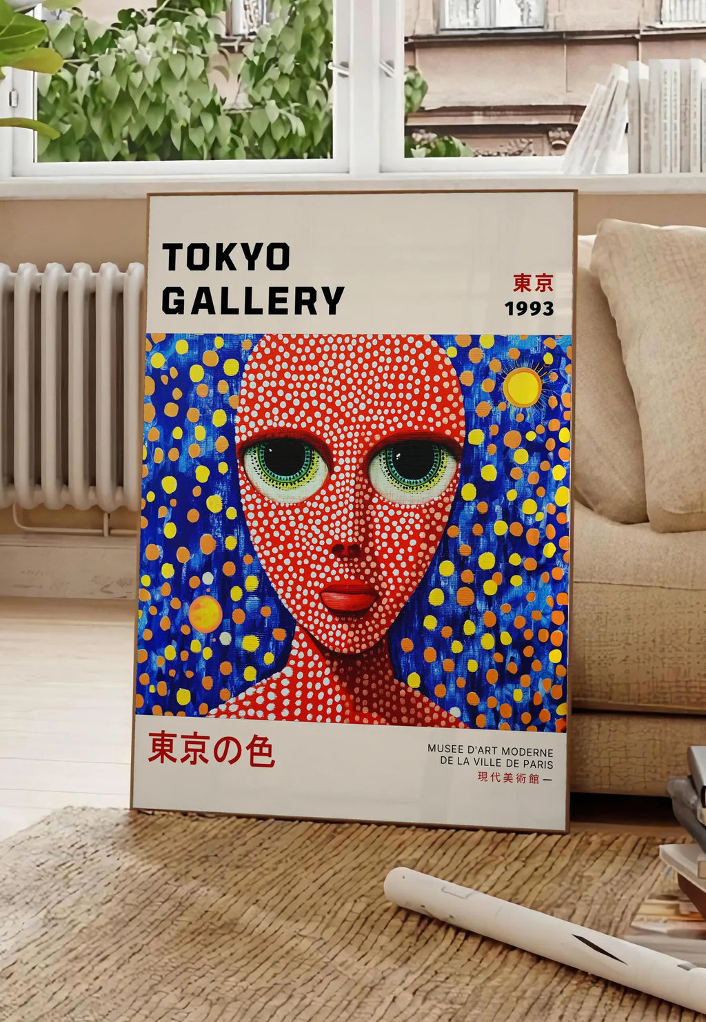 Poster affiche visage de femme a pois de Kusama art japonais, posee au sol dans un salon parisien, devant une grande fenetre donnant sur un immeuble haussmannien, entre un ficus et un canape creme