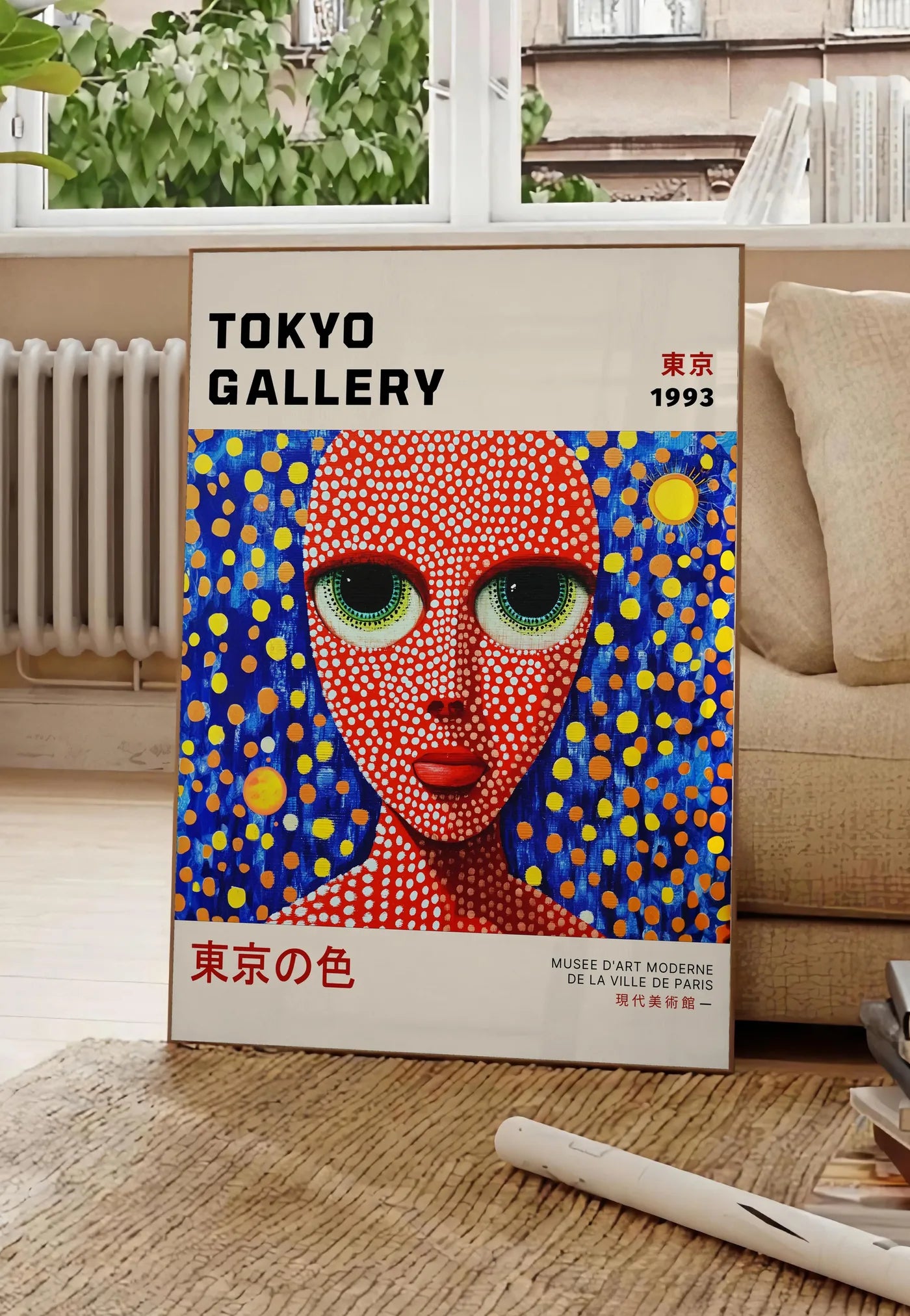 Poster affiche visage de femme a pois de Kusama art japonais, posee au sol dans un salon parisien, devant une grande fenetre donnant sur un immeuble haussmannien, entre un ficus et un canape creme