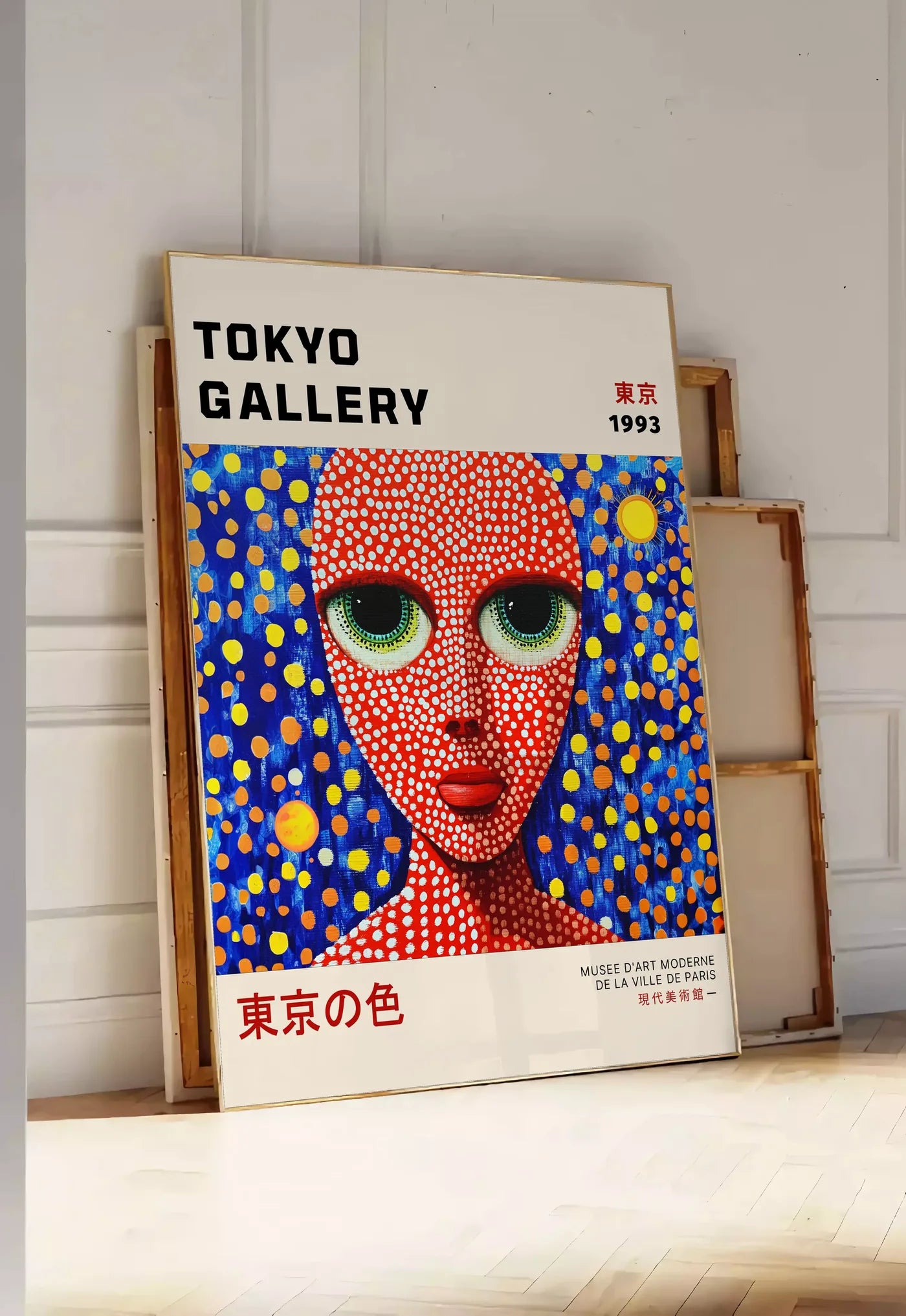 Tirage encadrable affiche visage de femme a pois de Kusama art japonais, posee au sol dans une entree lumineuse, contre un mur a panneaux blancs, a cote de chassis en bois empiles
