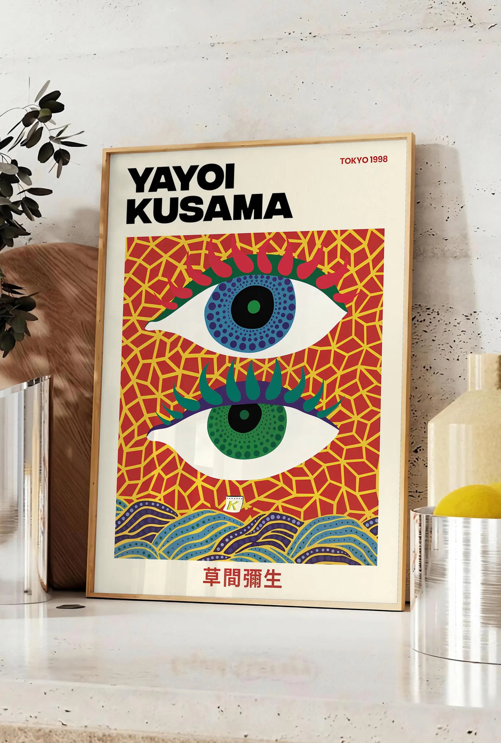 Affiche affiche yeux a pois de Kusama art japonais, posee sur un plan de travail de cuisine en pierre claire, entre une branche d'eucalyptus en vase et un bocal de citrons