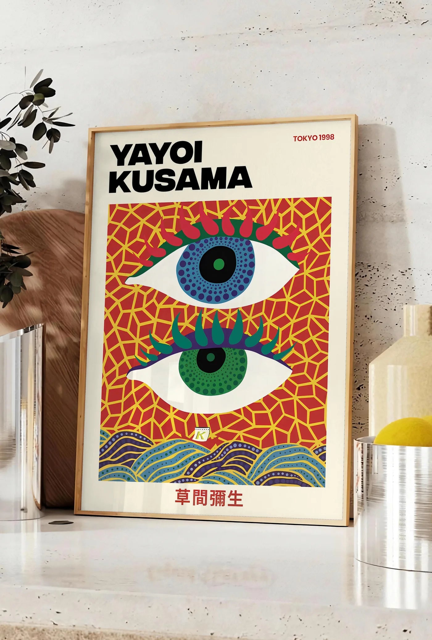 Affiche affiche yeux a pois de Kusama art japonais, posee sur un plan de travail de cuisine en pierre claire, entre une branche d'eucalyptus en vase et un bocal de citrons