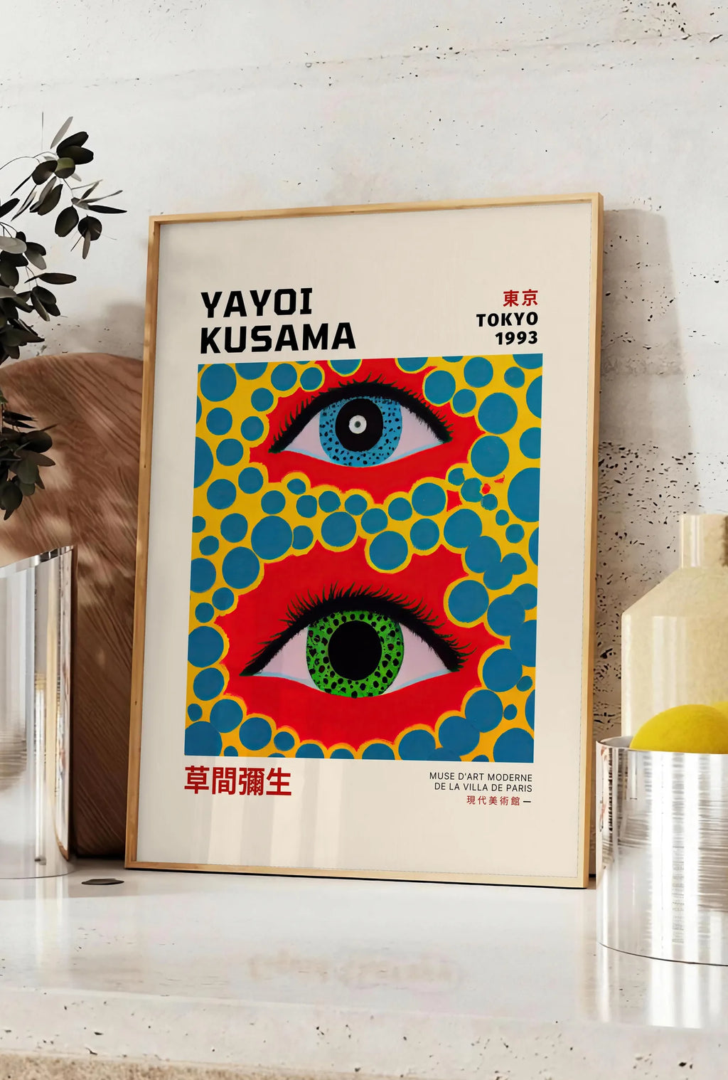 Affiche affiche yeux a pois jaune de Kusama art japonais, posee sur un plan de travail de cuisine en pierre claire, entre une branche d'eucalyptus en vase et un bocal de citrons