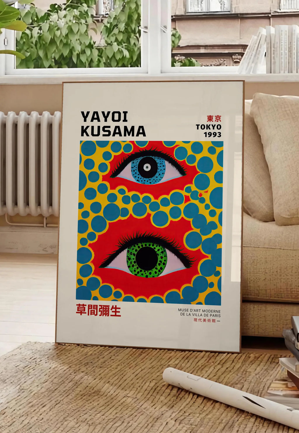 Poster affiche yeux a pois jaune de Kusama art japonais, posee au sol dans un salon parisien, devant une grande fenetre donnant sur un immeuble haussmannien, entre un ficus et un canape creme