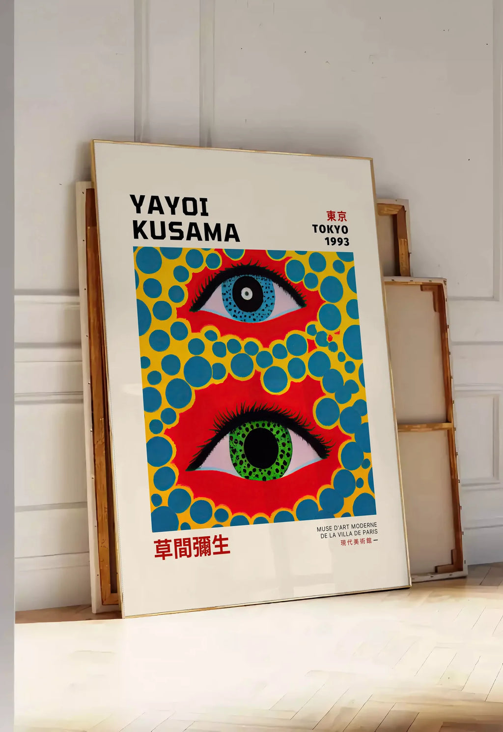 Tirage encadrable affiche yeux a pois jaune de Kusama art japonais, posee au sol dans une entree lumineuse, contre un mur a panneaux blancs, a cote de chassis en bois empiles