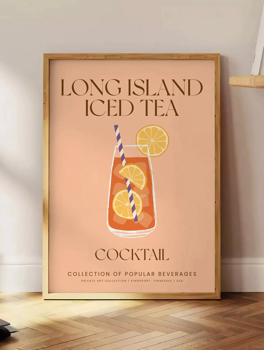 Estampe affiche cocktail Long Island Iced Tea, posee au sol dans un coin salon, sur un parquet a chevrons, pres d'une table d'appoint en chene chargee de livres