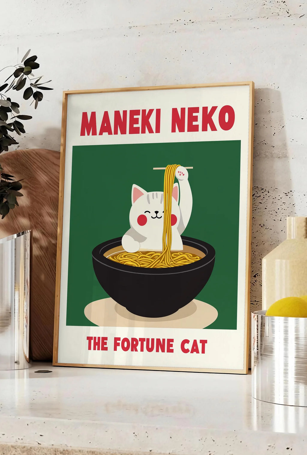 Affiche affiche Maneki Neko chat soulevant des ramen a la baguette derriere un bol noir, posee sur un plan de travail de cuisine en pierre claire, entre une branche d'eucalyptus en vase et un bocal de citrons