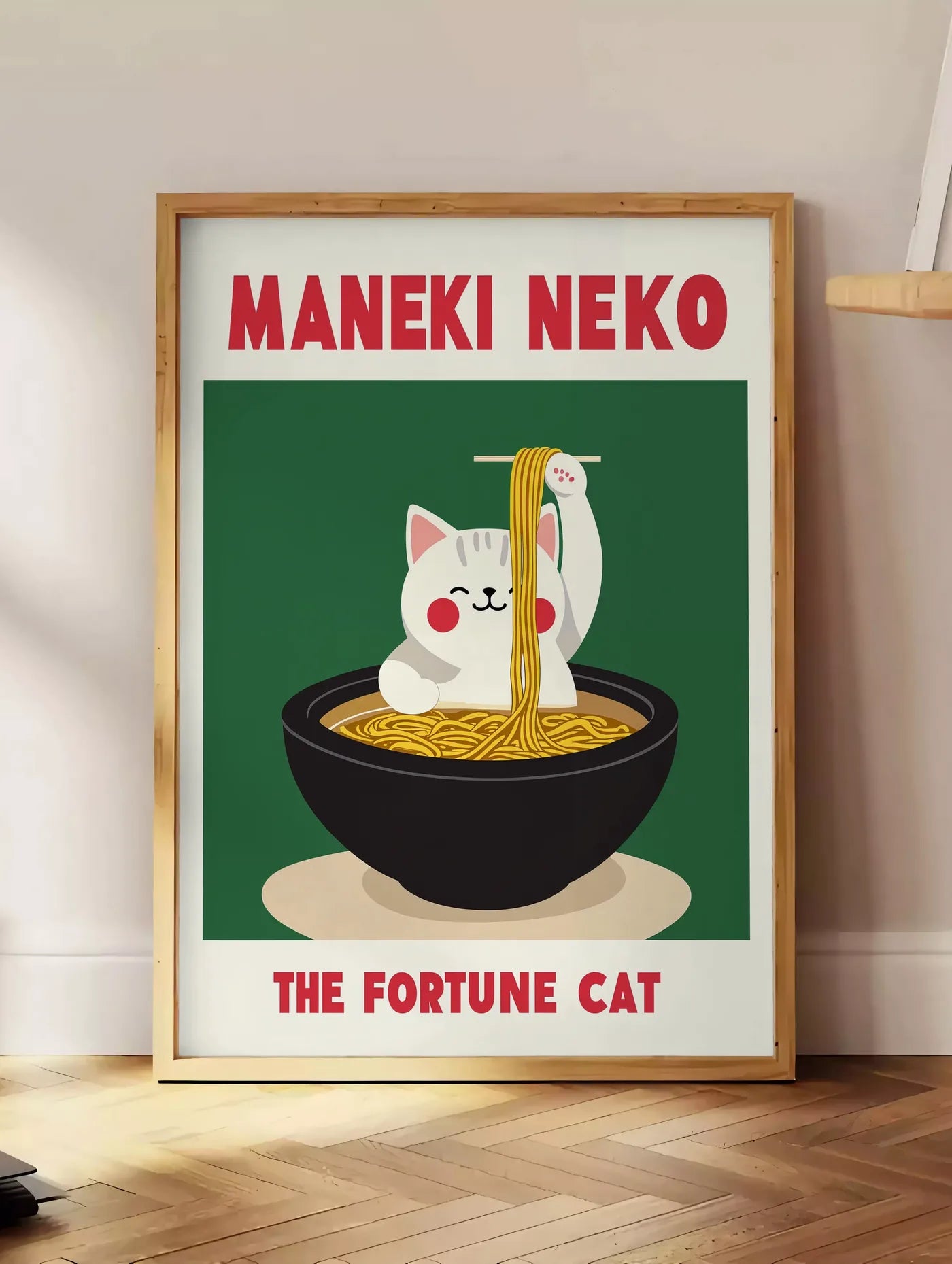 Estampe affiche Maneki Neko chat soulevant des ramen a la baguette derriere un bol noir, posee au sol dans un coin salon, sur un parquet a chevrons, pres d'une table d'appoint en chene chargee de livres