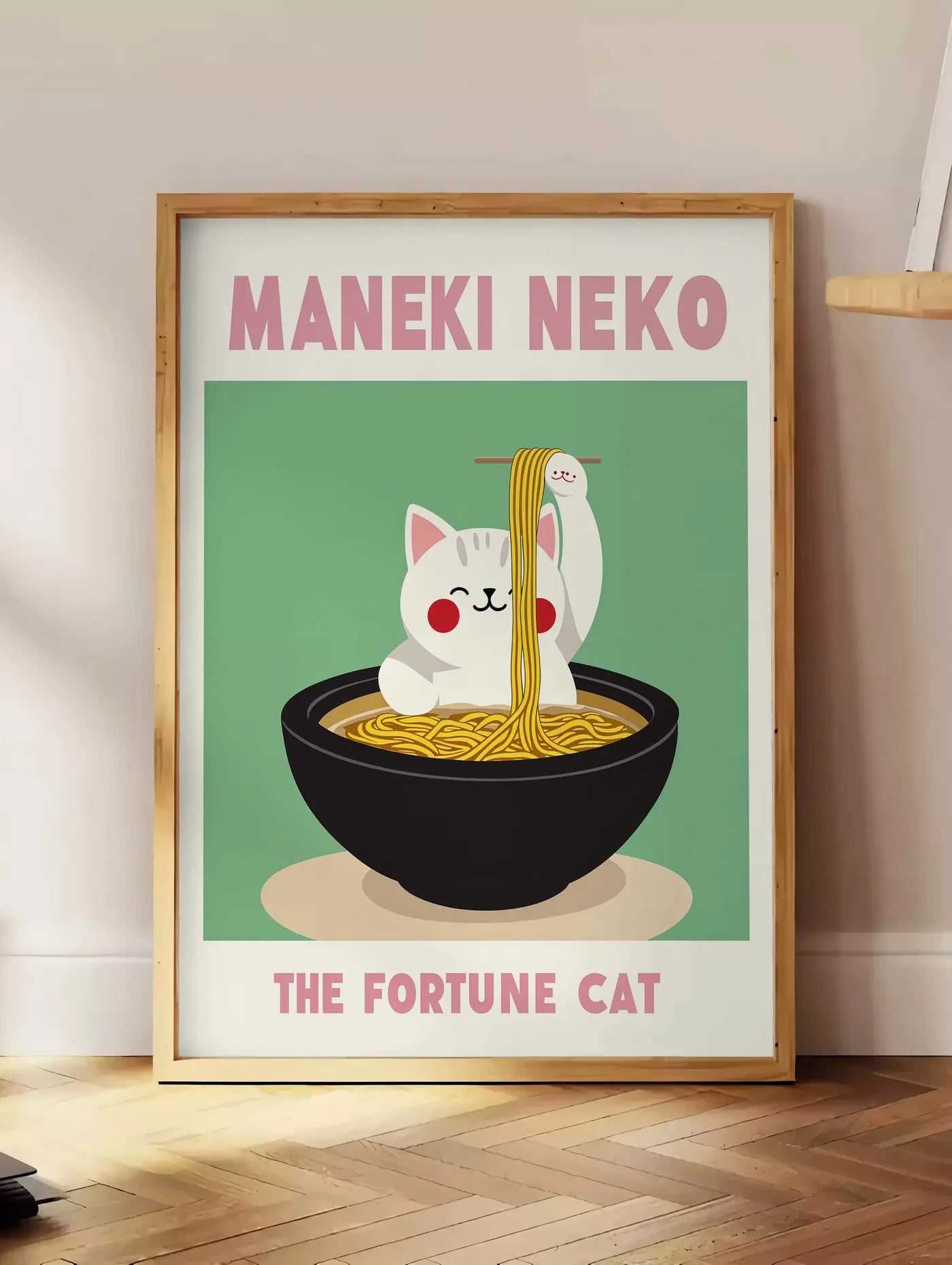 Estampe affiche Maneki Neko chat et ramen sur fond vert sauge, posee au sol dans un coin salon, sur un parquet a chevrons, pres d'une table d'appoint en chene chargee de livres