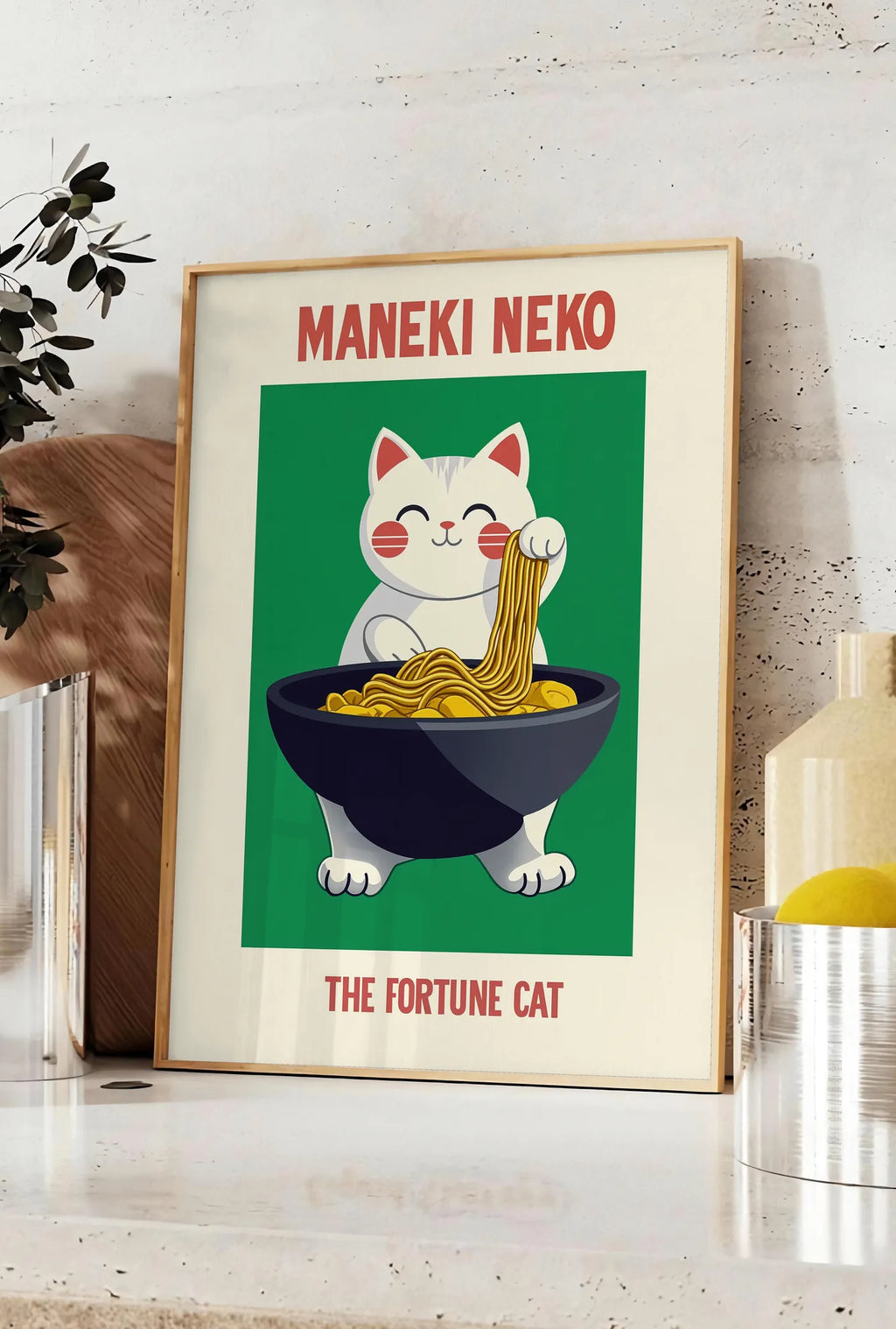 Affiche affiche Maneki Neko chat porte-bonheur attrapant des ramen au-dessus d'un bol noir, posee sur un plan de travail de cuisine en pierre claire, entre une branche d'eucalyptus en vase et un bocal de citrons