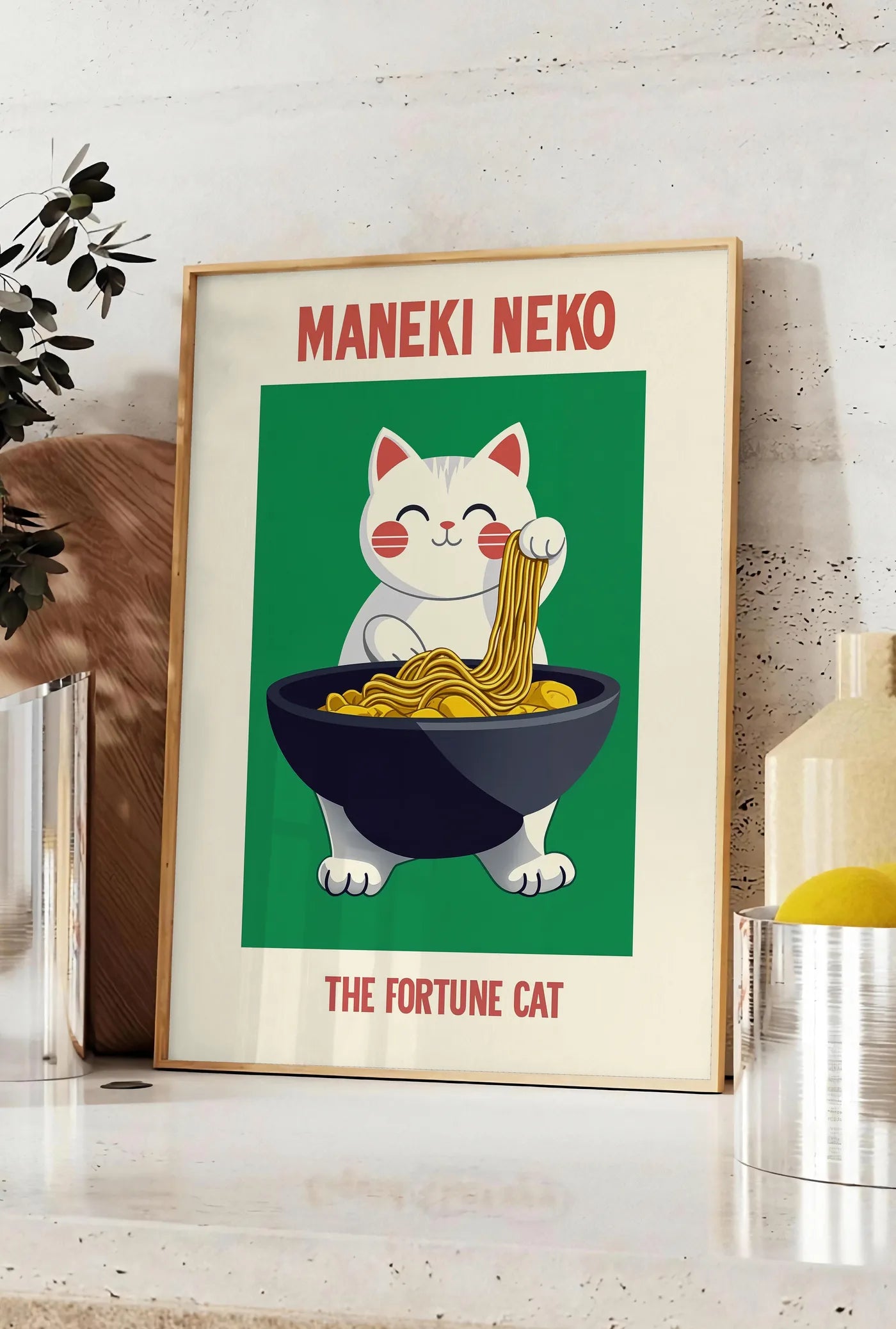 Affiche affiche Maneki Neko chat porte-bonheur attrapant des ramen au-dessus d'un bol noir, posee sur un plan de travail de cuisine en pierre claire, entre une branche d'eucalyptus en vase et un bocal de citrons