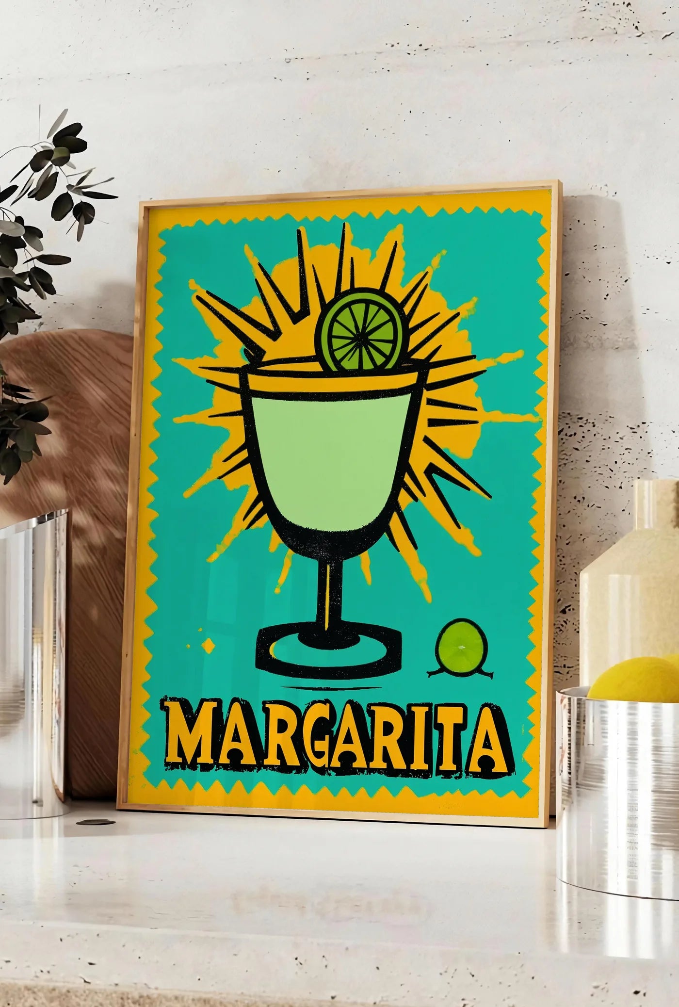 Affiche affiche cocktail Margarita pop art, posee sur un plan de travail de cuisine en pierre claire, entre une branche d'eucalyptus en vase et un bocal de citrons