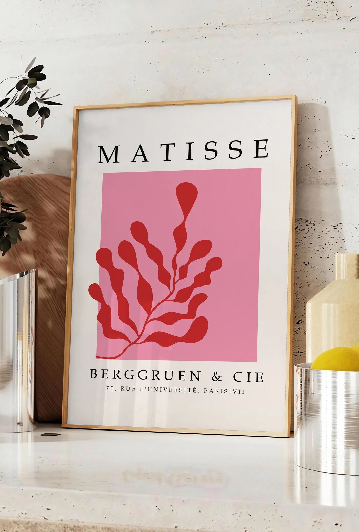 Affiche algue Rouge sur Rose en papiers decoupes Matisse sur fond colore, posee sur un plan de travail de cuisine en pierre claire, entre une branche d'eucalyptus en vase et un bocal de citrons