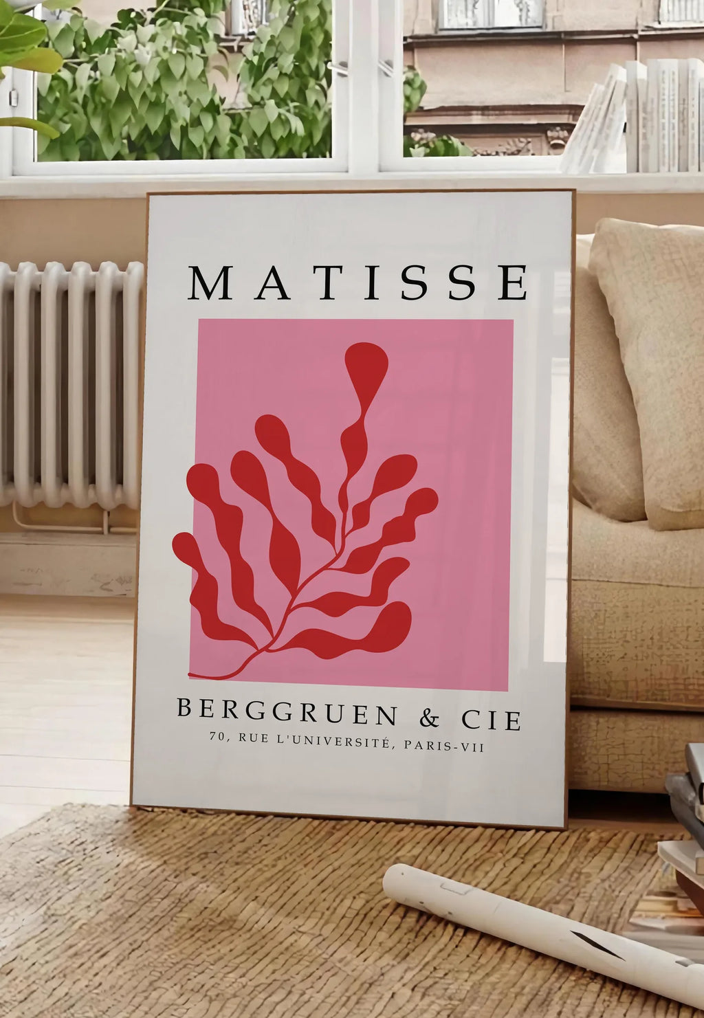 Poster algue Rouge sur Rose en papiers decoupes Matisse sur fond colore, posee au sol dans un salon parisien, devant une grande fenetre donnant sur un immeuble haussmannien, entre un ficus et un canape creme