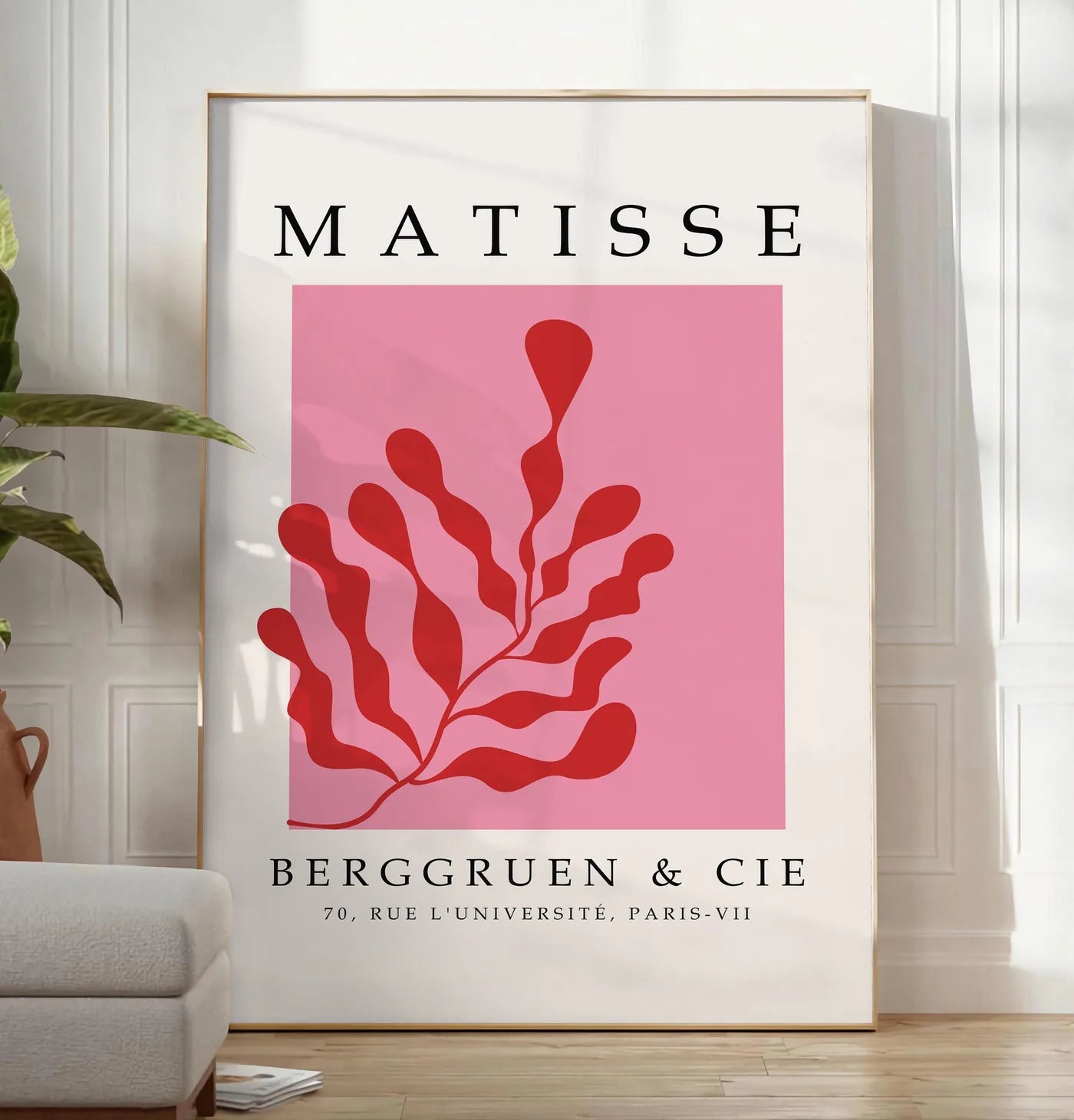 Reproduction algue Rouge sur Rose en papiers decoupes Matisse sur fond colore, posee au sol dans un salon minimaliste clair, a cote d'un canape beige et d'une plante verte, sur un parquet clair