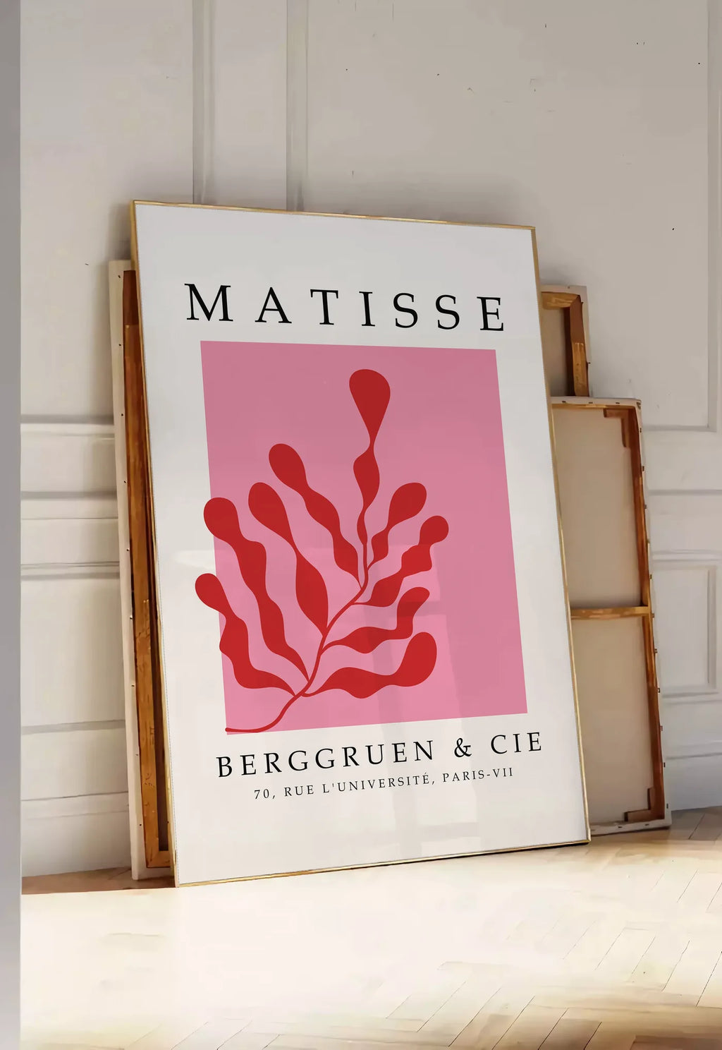 Tirage encadrable algue Rouge sur Rose en papiers decoupes Matisse sur fond colore, posee au sol dans une entree lumineuse, contre un mur a panneaux blancs, a cote de chassis en bois empiles