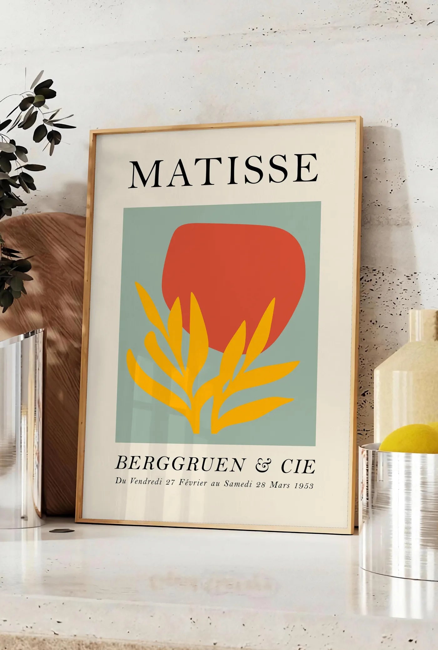 Affiche forme Rouge et Feuille Jaune en papiers decoupes Matisse sur fond colore, posee sur un plan de travail de cuisine en pierre claire, entre une branche d'eucalyptus en vase et un bocal de citrons