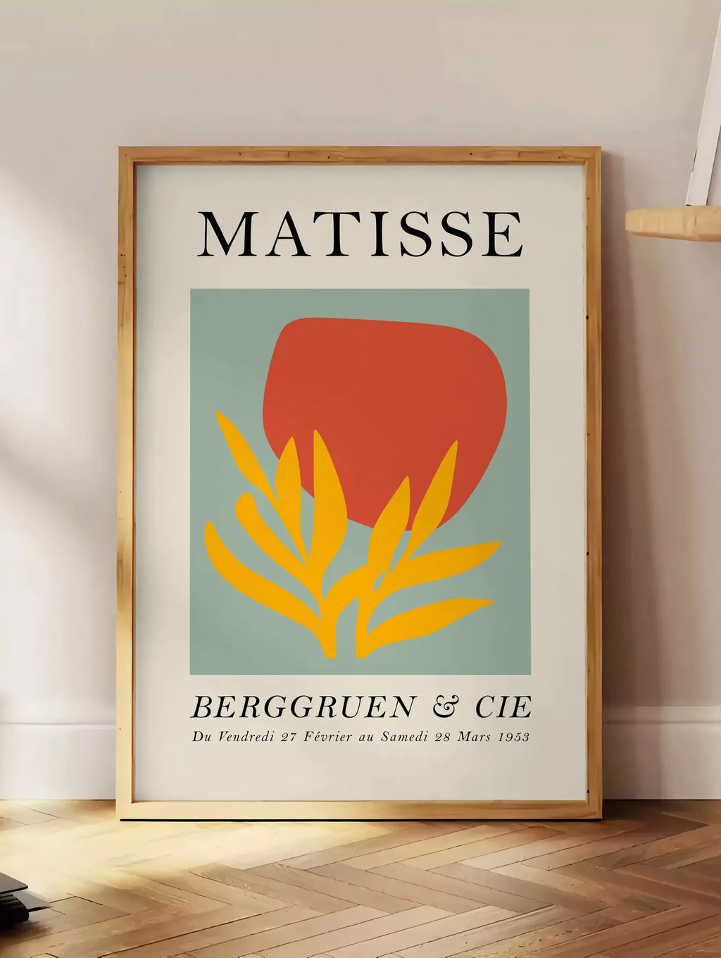 Estampe forme Rouge et Feuille Jaune en papiers decoupes Matisse sur fond colore, posee au sol dans un coin salon, sur un parquet a chevrons, pres d'une table d'appoint en chene chargee de livres