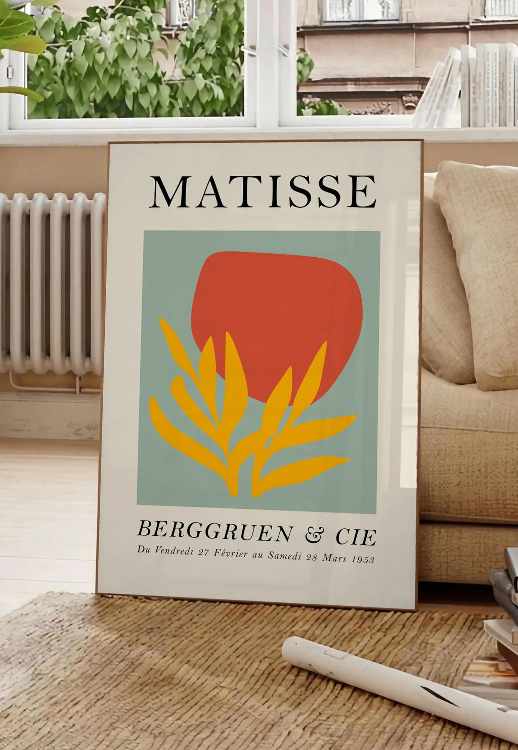 Poster forme Rouge et Feuille Jaune en papiers decoupes Matisse sur fond colore, posee au sol dans un salon parisien, devant une grande fenetre donnant sur un immeuble haussmannien, entre un ficus et un canape creme
