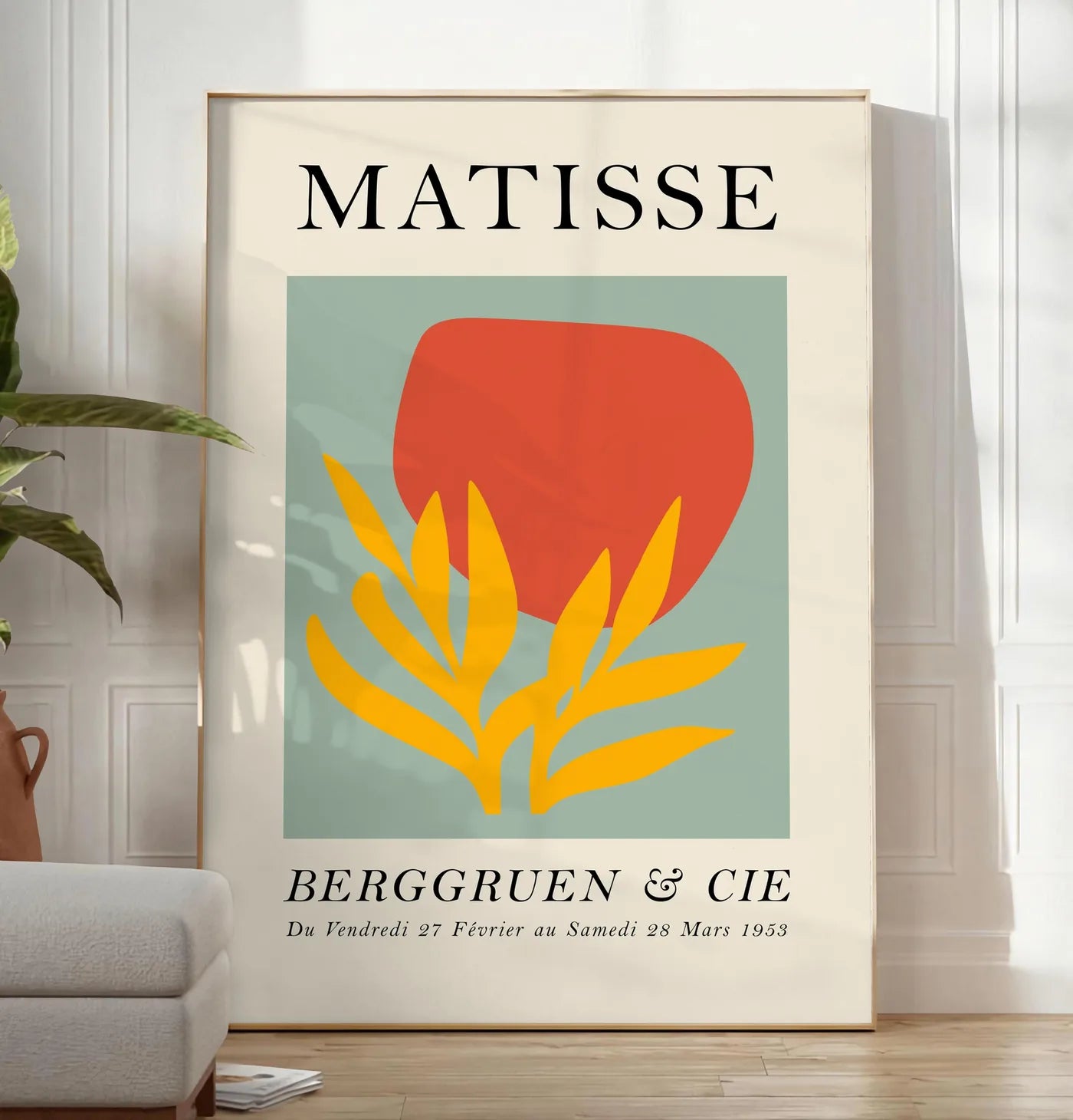 Reproduction forme Rouge et Feuille Jaune en papiers decoupes Matisse sur fond colore, posee au sol dans un salon minimaliste clair, a cote d'un canape beige et d'une plante verte, sur un parquet clair