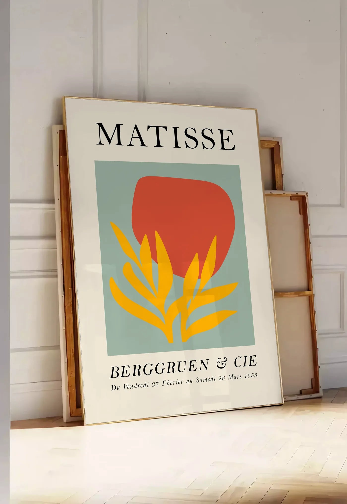 Tirage encadrable forme Rouge et Feuille Jaune en papiers decoupes Matisse sur fond colore, posee au sol dans une entree lumineuse, contre un mur a panneaux blancs, a cote de chassis en bois empiles