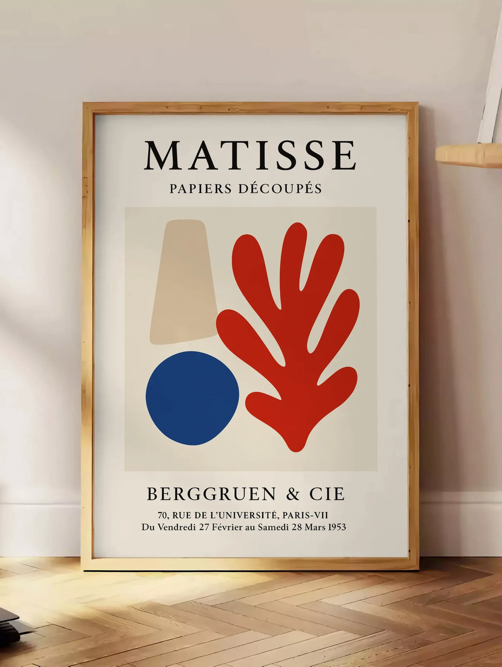 Estampe cone beige cercle bleu et corail rouge sur fond creme, posee au sol dans un coin salon, sur un parquet a chevrons, pres d'une table d'appoint en chene chargee de livres