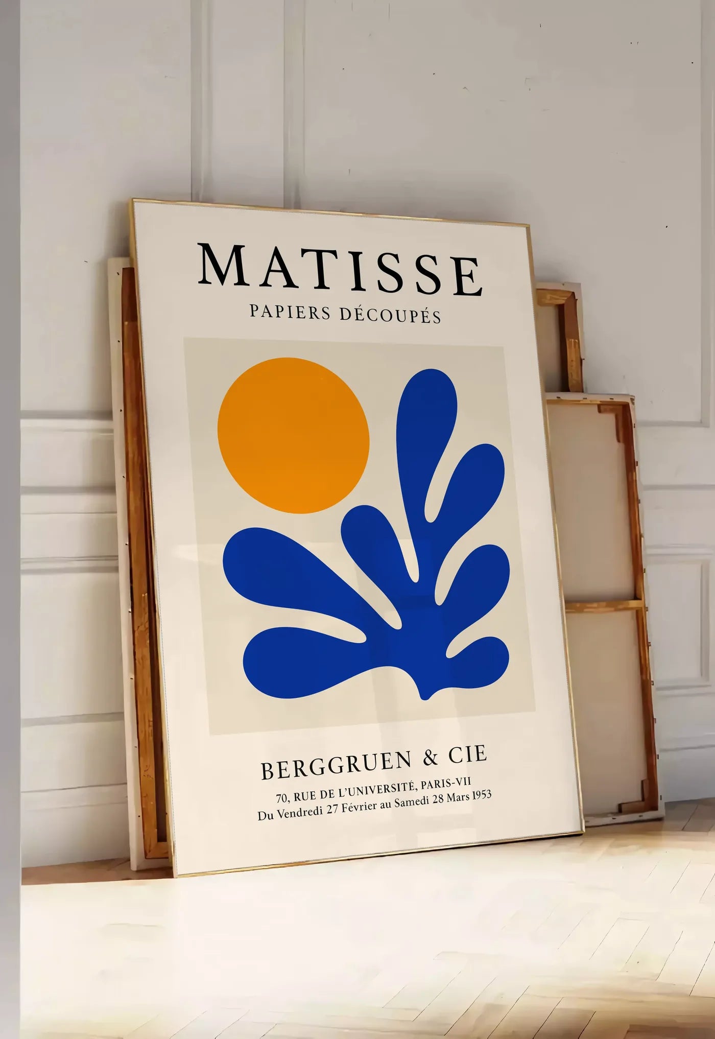 Tirage encadrable corail Bleu et Soleil Orange en papiers decoupes Matisse sur fond colore, posee au sol dans une entree lumineuse, contre un mur a panneaux blancs, a cote de chassis en bois empiles