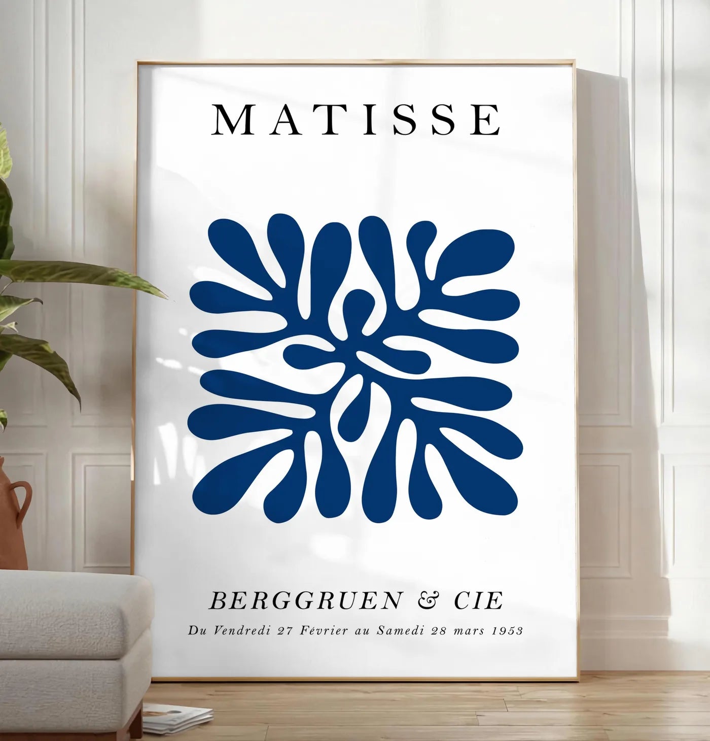 Reproduction corail Bleu Symetrique en papiers decoupes Matisse sur fond colore, posee au sol dans un salon minimaliste clair, a cote d'un canape beige et d'une plante verte, sur un parquet clair