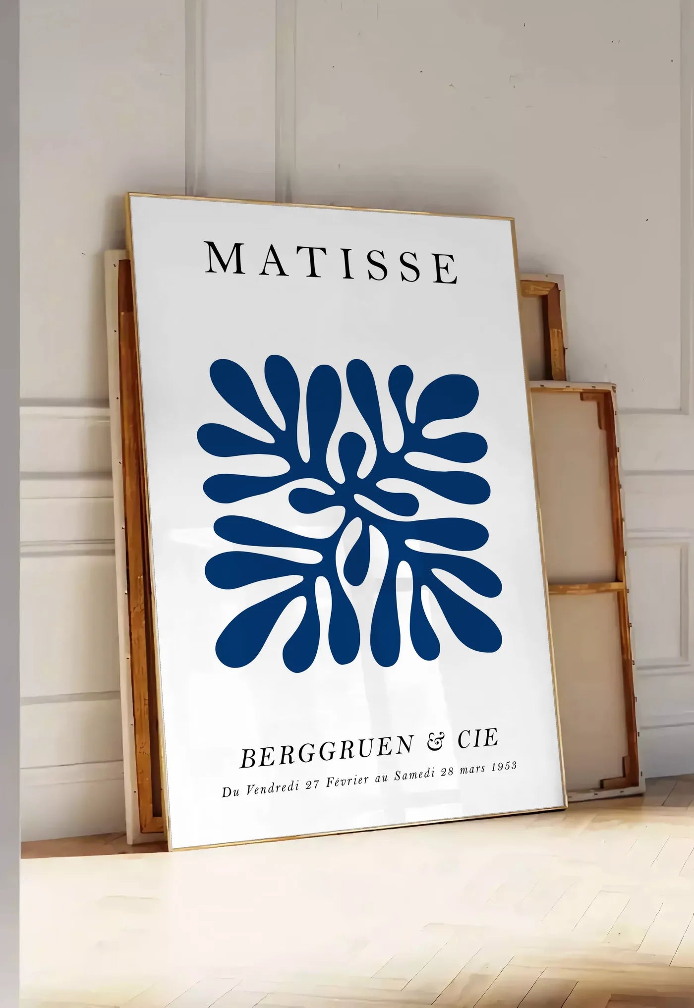Tirage encadrable corail Bleu Symetrique en papiers decoupes Matisse sur fond colore, posee au sol dans une entree lumineuse, contre un mur a panneaux blancs, a cote de chassis en bois empiles
