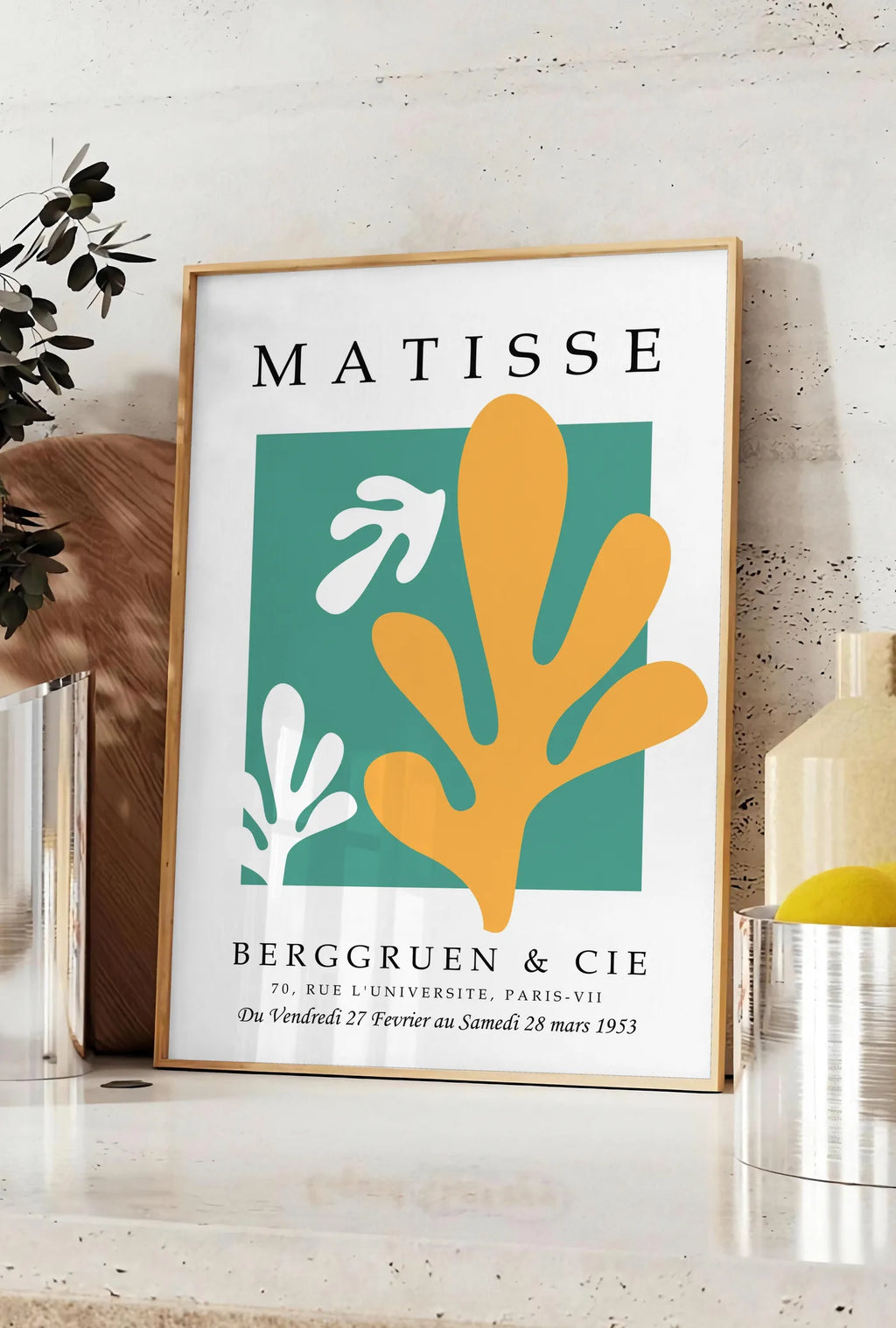 Affiche corail Jaune sur Vert en papiers decoupes Matisse sur fond colore, posee sur un plan de travail de cuisine en pierre claire, entre une branche d'eucalyptus en vase et un bocal de citrons