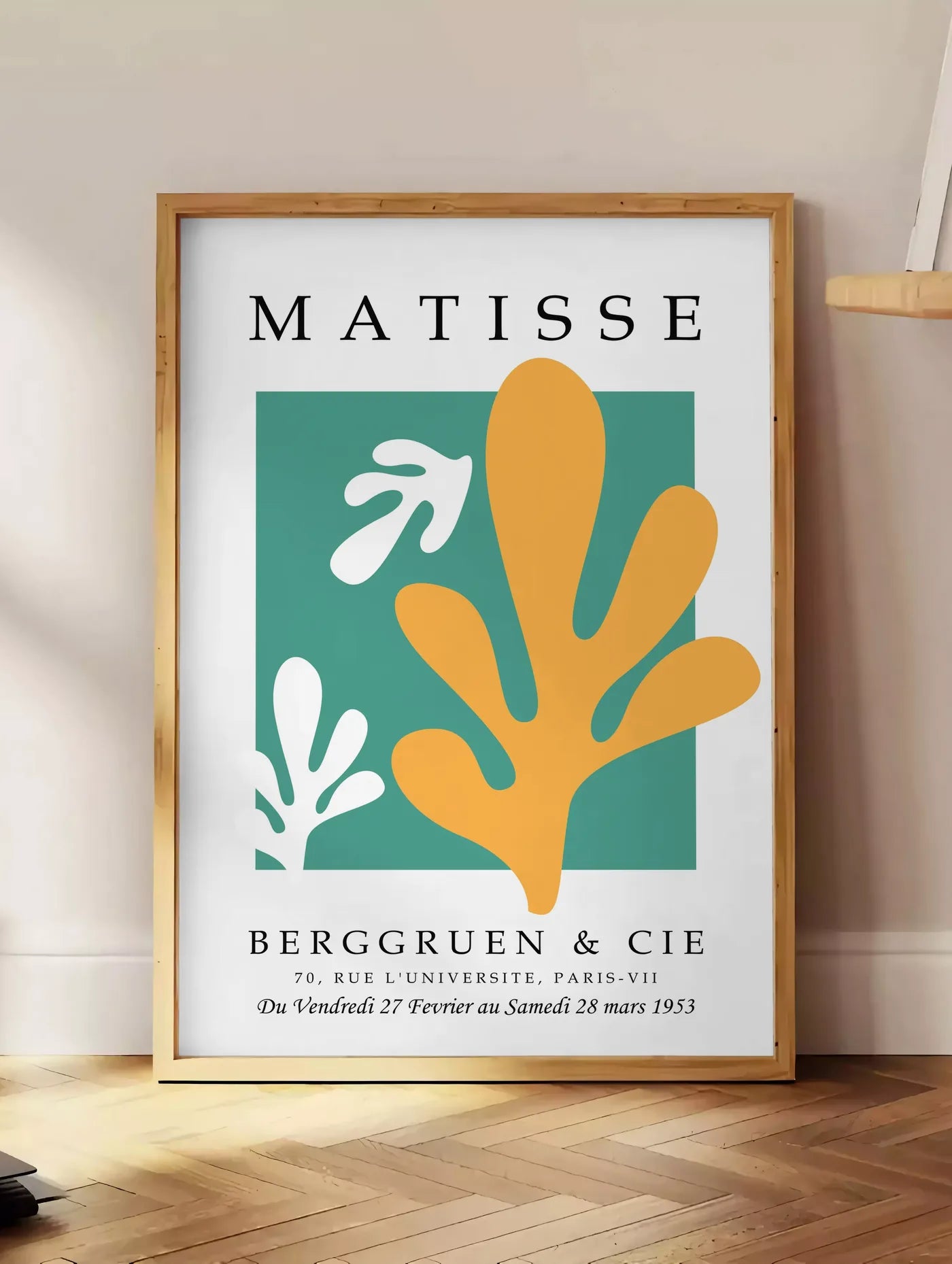 Estampe corail Jaune sur Vert en papiers decoupes Matisse sur fond colore, posee au sol dans un coin salon, sur un parquet a chevrons, pres d'une table d'appoint en chene chargee de livres