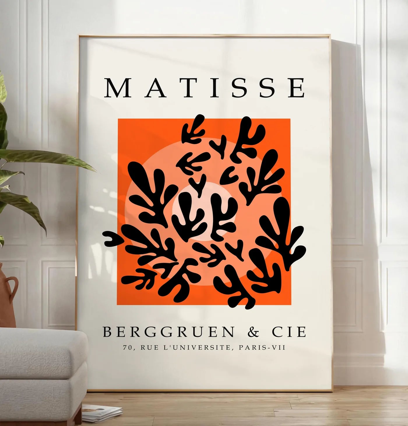 Reproduction corail Noir sur Orange en papiers decoupes Matisse sur fond colore, posee au sol dans un salon minimaliste clair, a cote d'un canape beige et d'une plante verte, sur un parquet clair