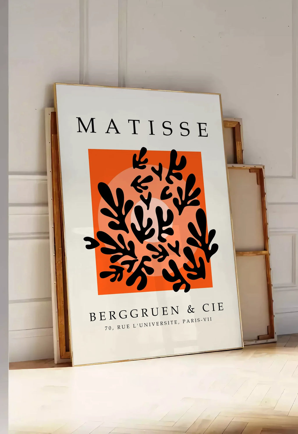 Tirage encadrable corail Noir sur Orange en papiers decoupes Matisse sur fond colore, posee au sol dans une entree lumineuse, contre un mur a panneaux blancs, a cote de chassis en bois empiles