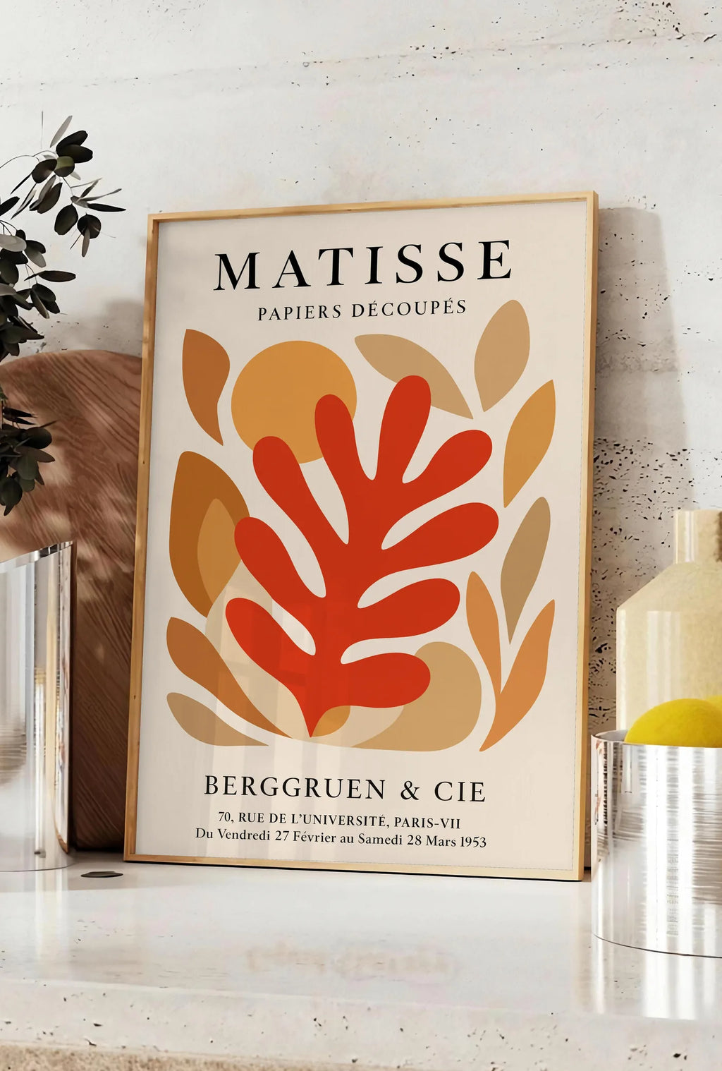 Affiche corail Rouge Tons Automne en papiers decoupes Matisse sur fond colore, posee sur un plan de travail de cuisine en pierre claire, entre une branche d'eucalyptus en vase et un bocal de citrons