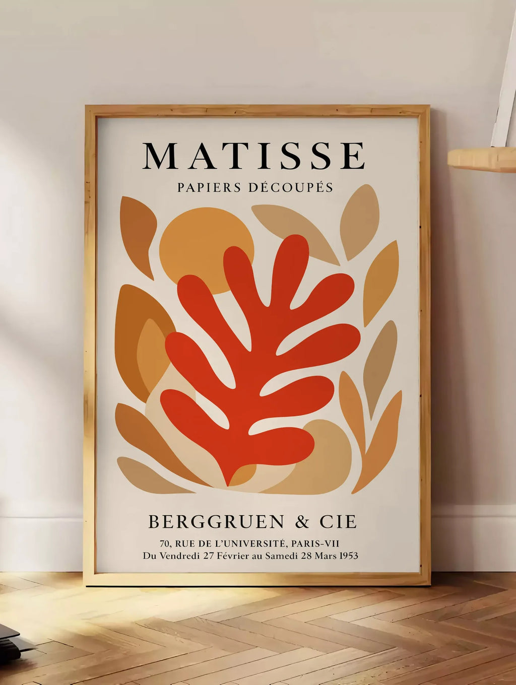 Estampe corail Rouge Tons Automne en papiers decoupes Matisse sur fond colore, posee au sol dans un coin salon, sur un parquet a chevrons, pres d'une table d'appoint en chene chargee de livres