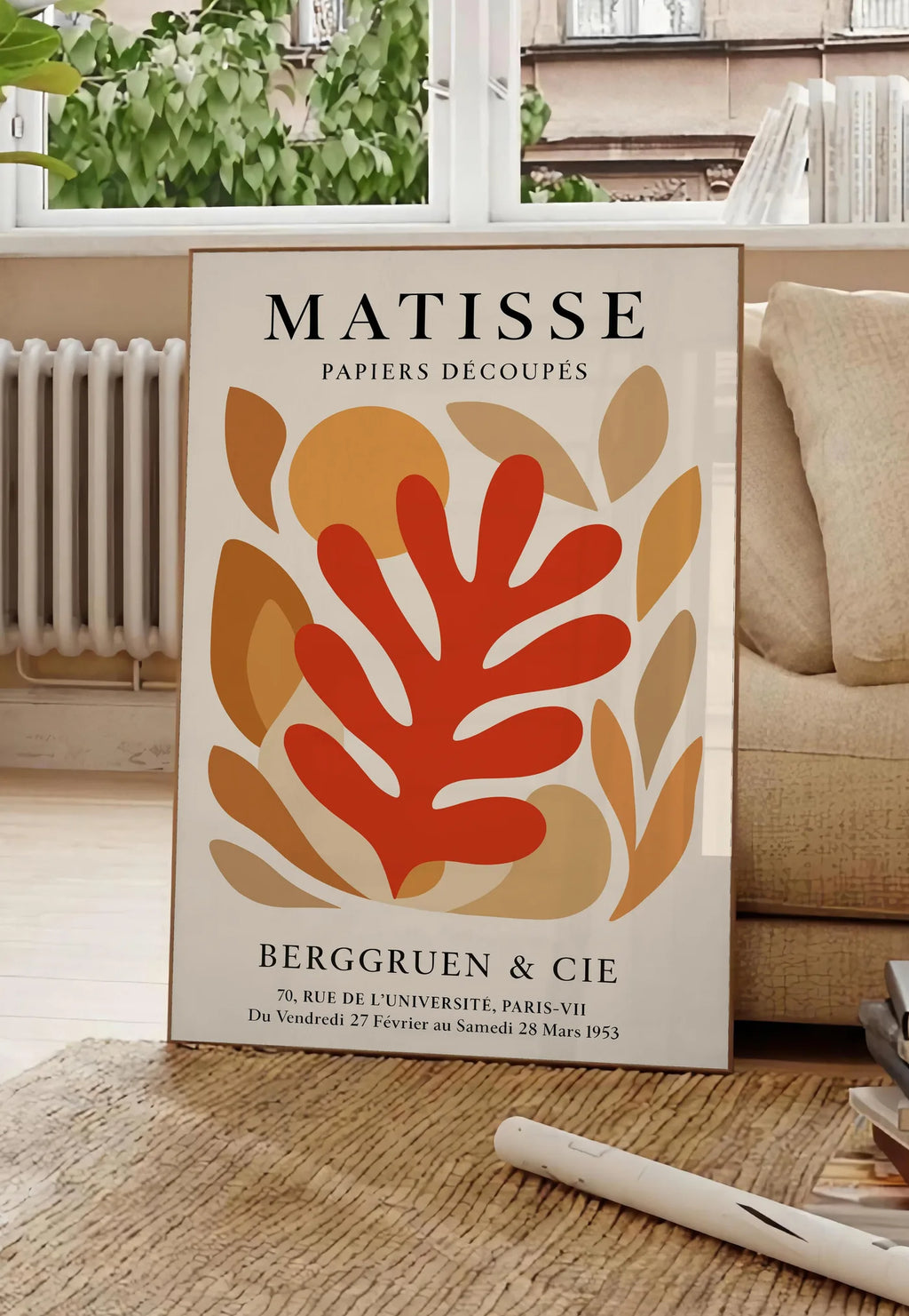Poster corail Rouge Tons Automne en papiers decoupes Matisse sur fond colore, posee au sol dans un salon parisien, devant une grande fenetre donnant sur un immeuble haussmannien, entre un ficus et un canape creme