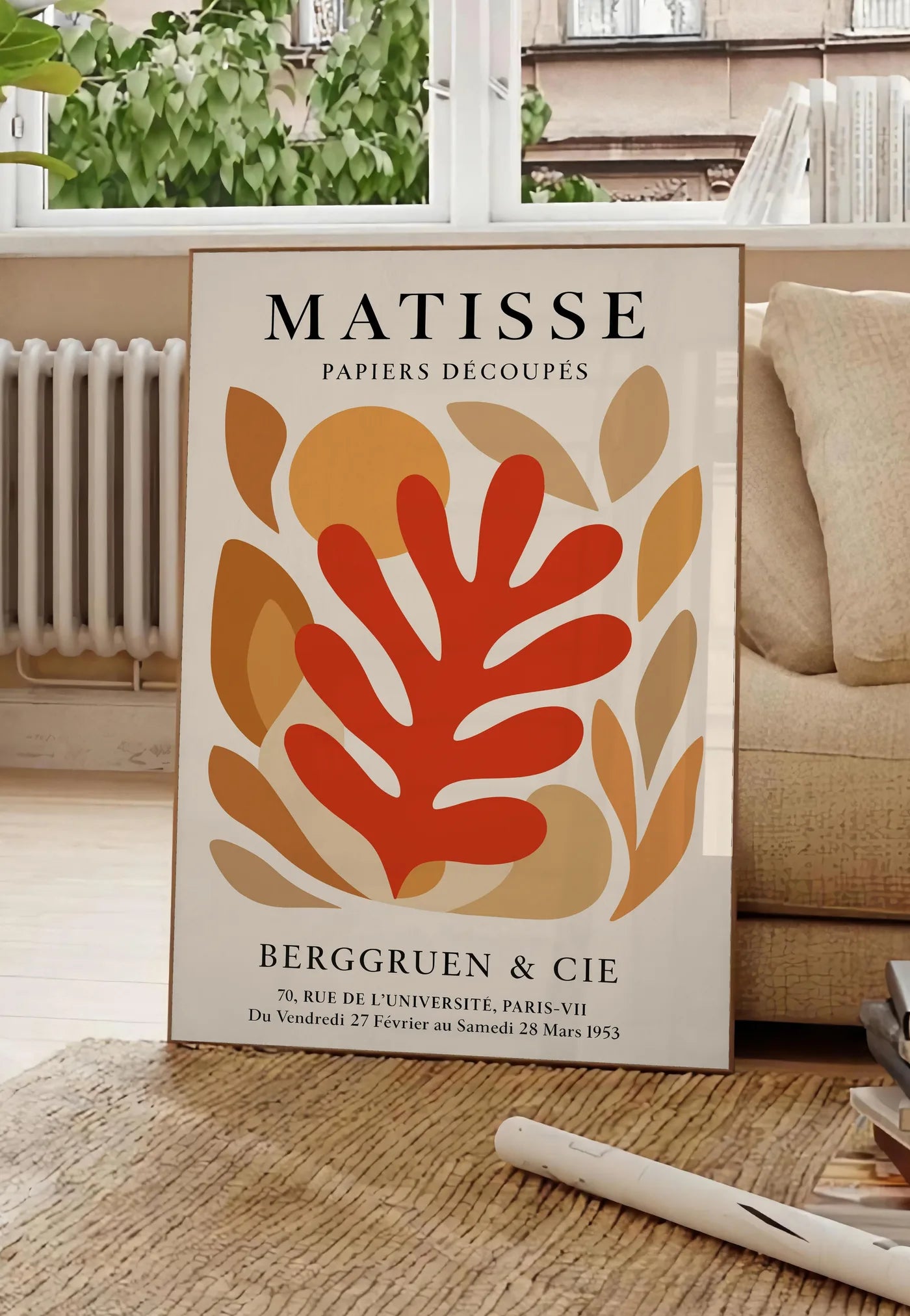 Poster corail Rouge Tons Automne en papiers decoupes Matisse sur fond colore, posee au sol dans un salon parisien, devant une grande fenetre donnant sur un immeuble haussmannien, entre un ficus et un canape creme