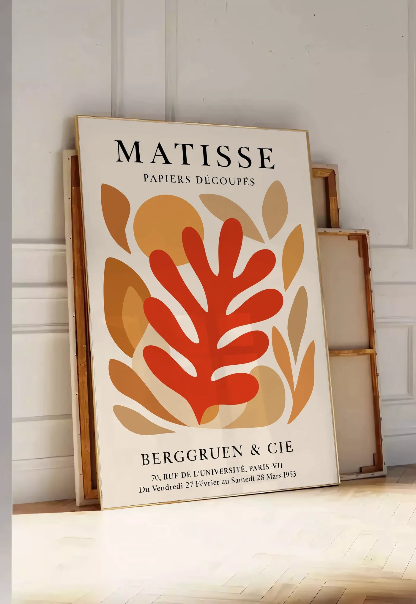 Tirage encadrable corail Rouge Tons Automne en papiers decoupes Matisse sur fond colore, posee au sol dans une entree lumineuse, contre un mur a panneaux blancs, a cote de chassis en bois empiles