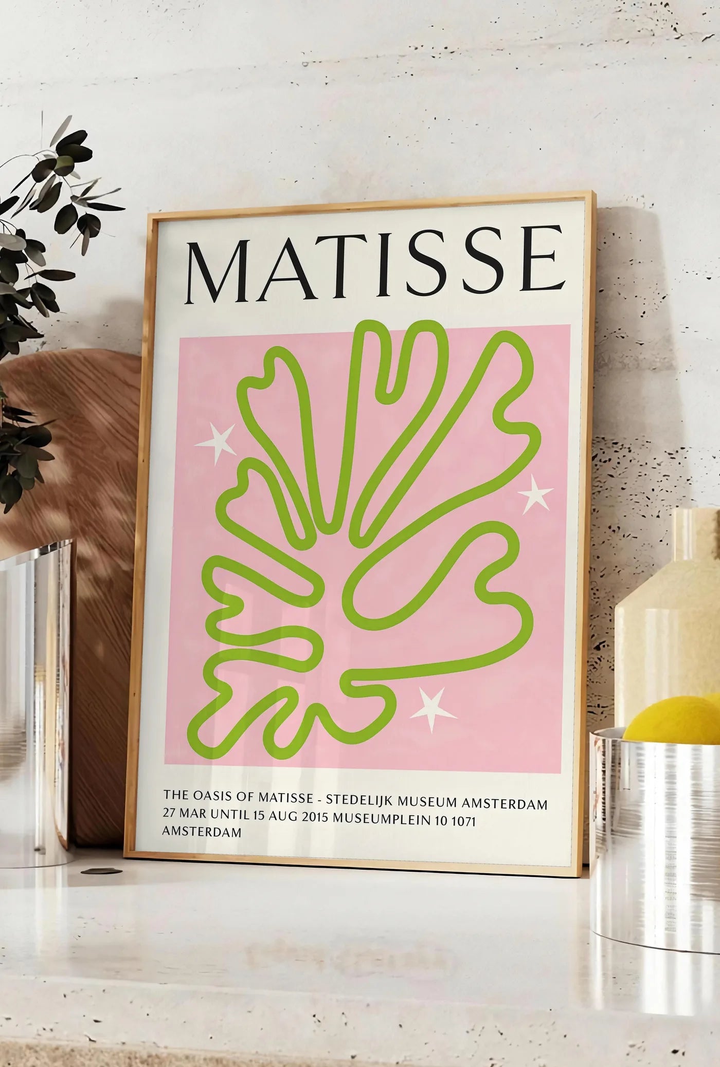 Affiche corail Vert Oasis en papiers decoupes Matisse sur fond colore, posee sur un plan de travail de cuisine en pierre claire, entre une branche d'eucalyptus en vase et un bocal de citrons