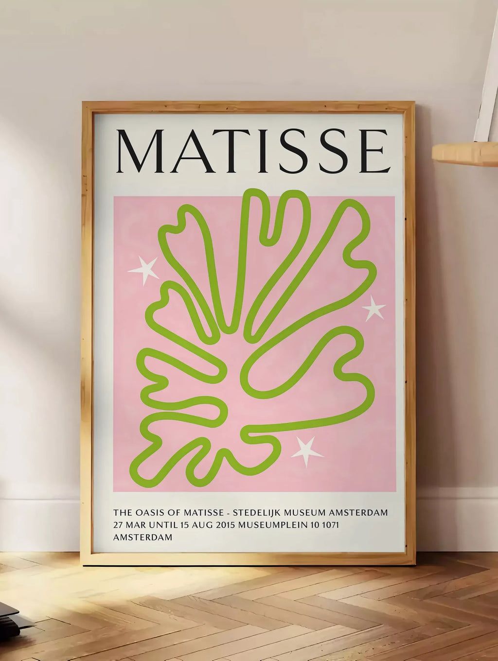 Estampe corail Vert Oasis en papiers decoupes Matisse sur fond colore, posee au sol dans un coin salon, sur un parquet a chevrons, pres d'une table d'appoint en chene chargee de livres