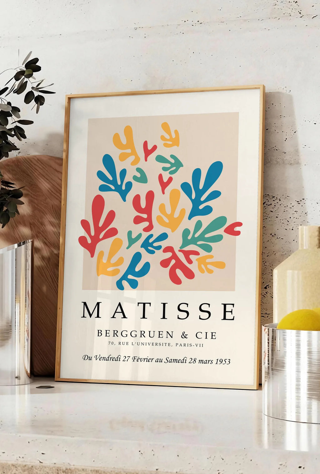 Affiche corails Multicolores en papiers decoupes Matisse sur fond colore, posee sur un plan de travail de cuisine en pierre claire, entre une branche d'eucalyptus en vase et un bocal de citrons