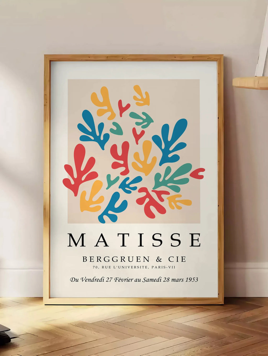 Estampe corails Multicolores en papiers decoupes Matisse sur fond colore, posee au sol dans un coin salon, sur un parquet a chevrons, pres d'une table d'appoint en chene chargee de livres