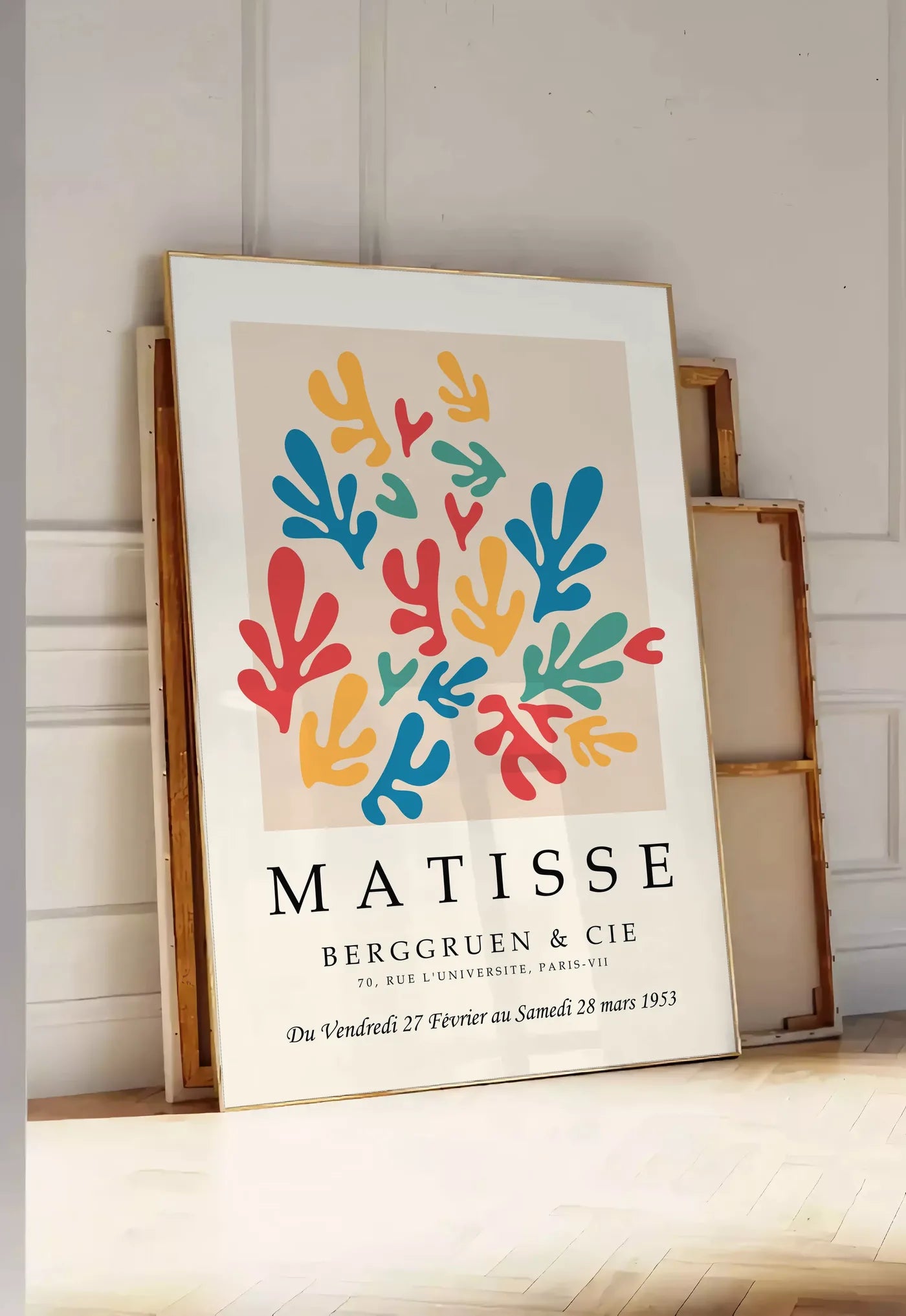 Tirage encadrable corails Multicolores en papiers decoupes Matisse sur fond colore, posee au sol dans une entree lumineuse, contre un mur a panneaux blancs, a cote de chassis en bois empiles